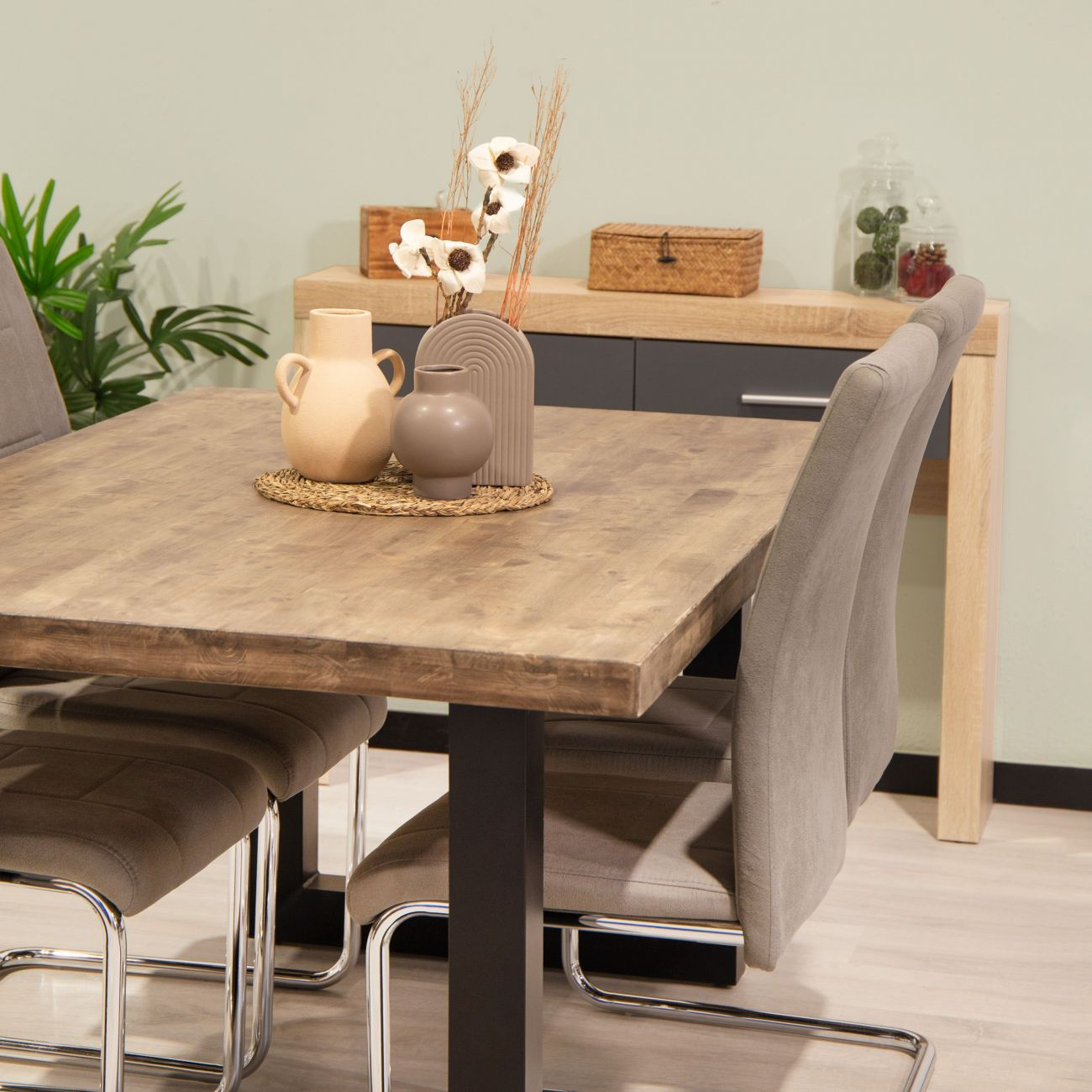 Mesa de madera con jarrones y sillas, junto a un aparador con decoración.
