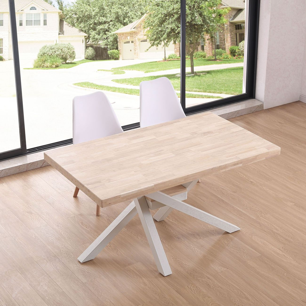 Mesa de madera clara y dos sillas blancas frente a una ventana con casas.