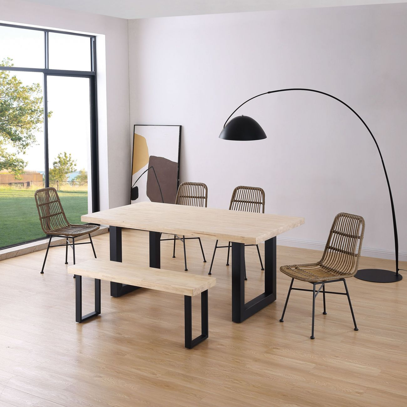 Una mesa de comedor de madera clara con patas negras, cuatro sillas de ratán y un banco de madera.