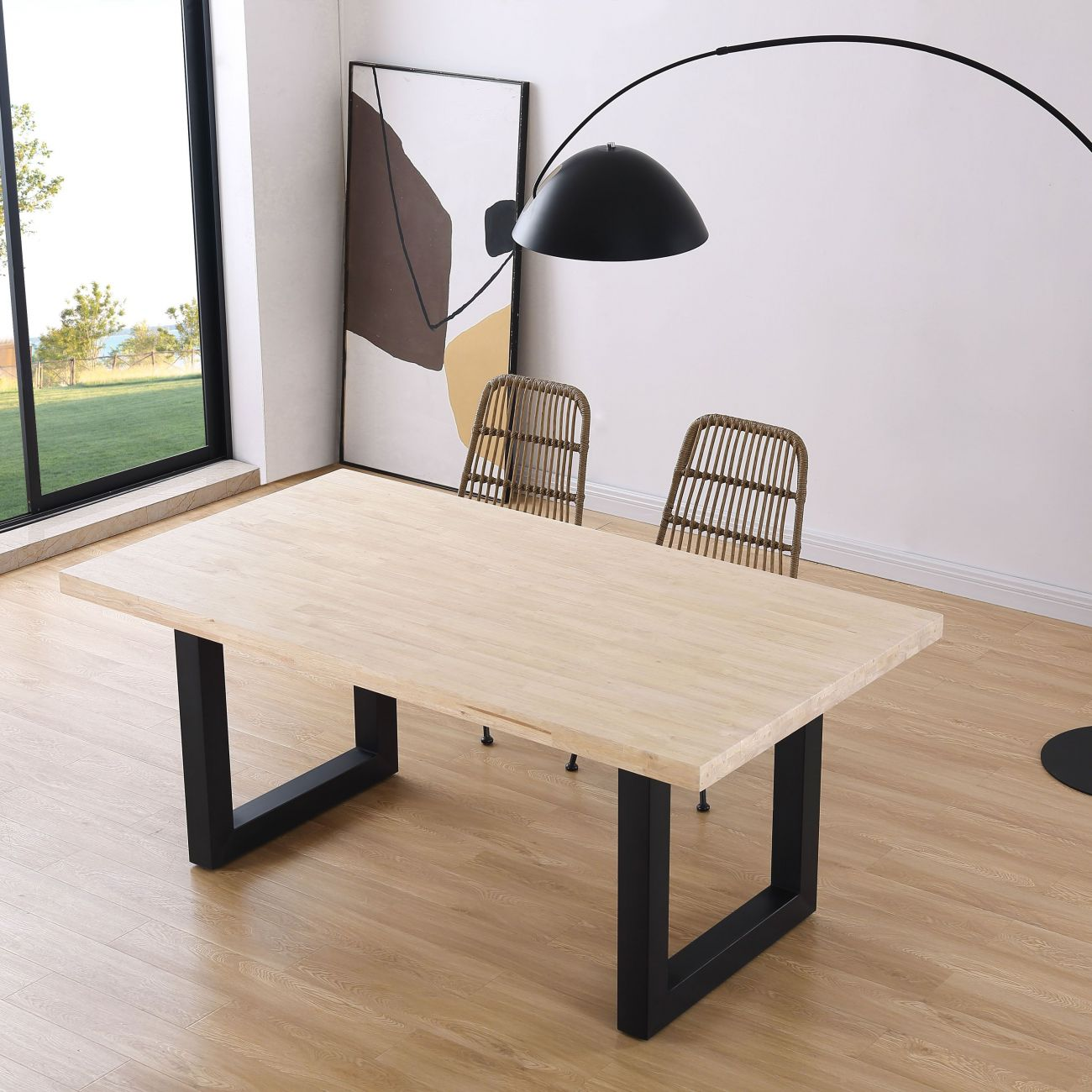 Una mesa de comedor de madera clara con patas de metal negro y dos sillas de ratán.
