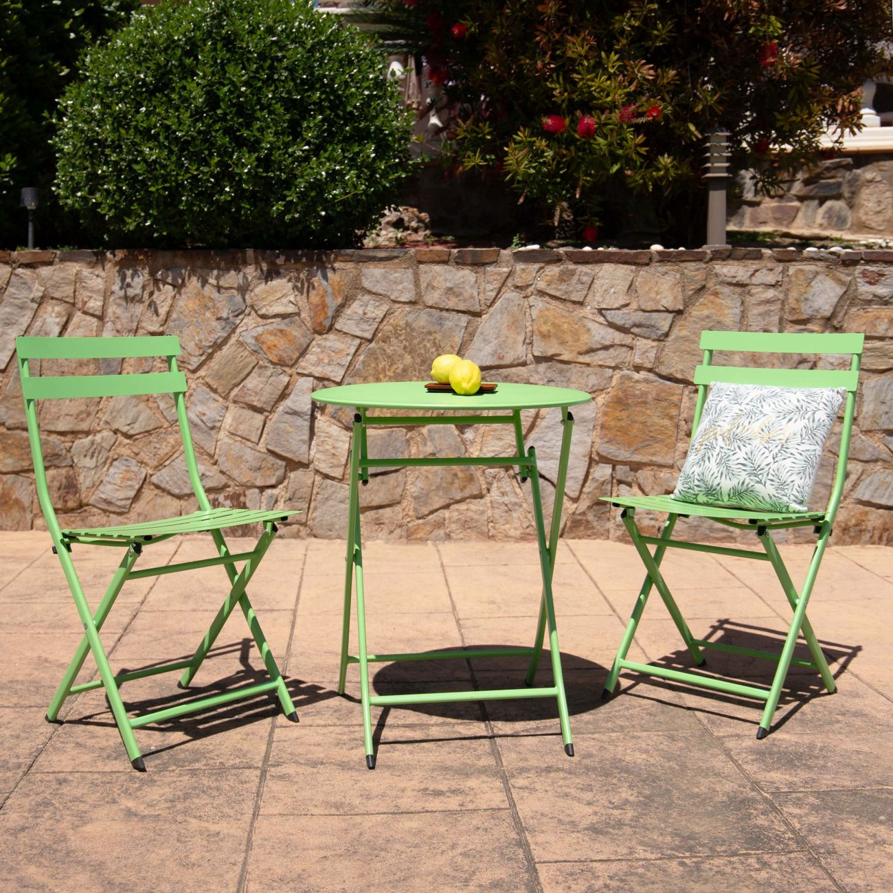 Dos sillas verdes de metal y una mesa redonda con dos limones en un patio.