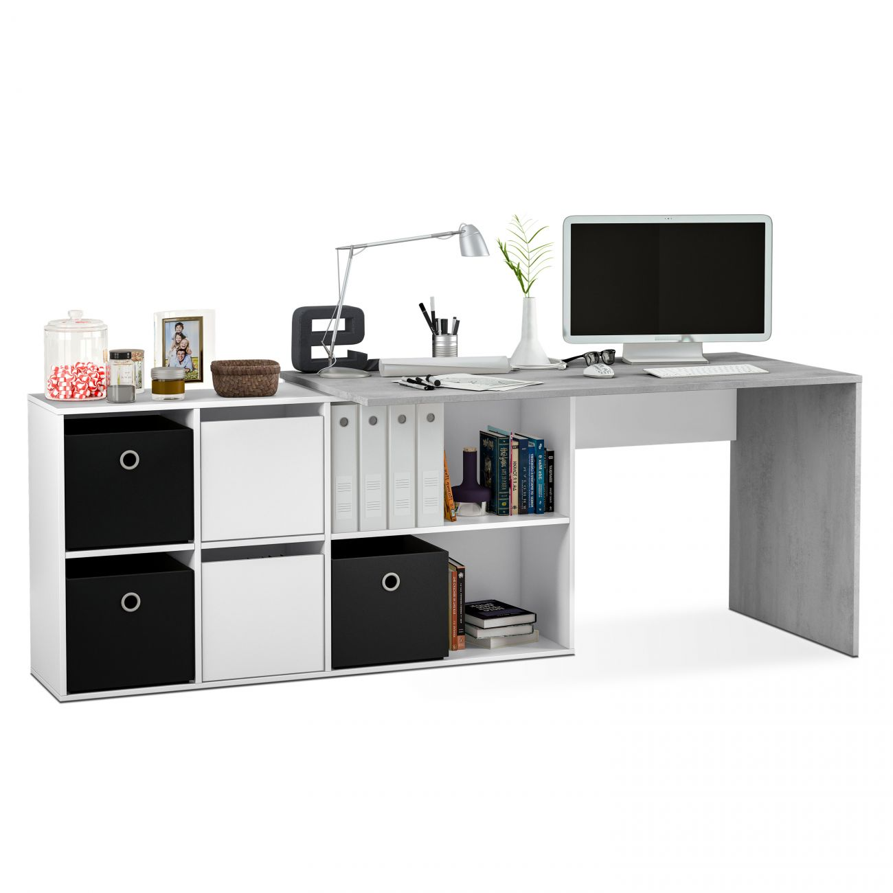 Un escritorio con computadora, lámpara, libros y cajas de almacenamiento.