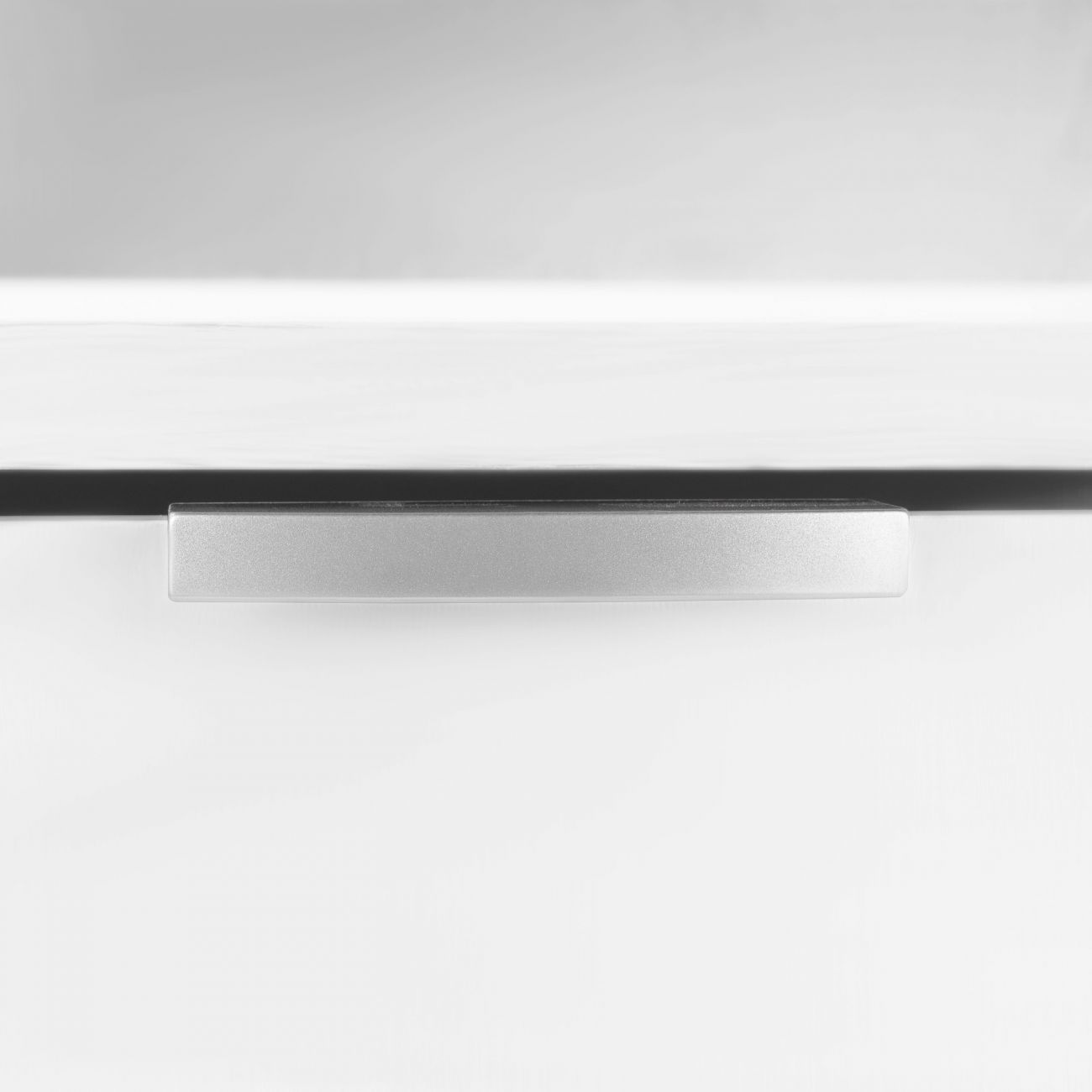 Un tirador plateado sobre una superficie blanca, con sombra.