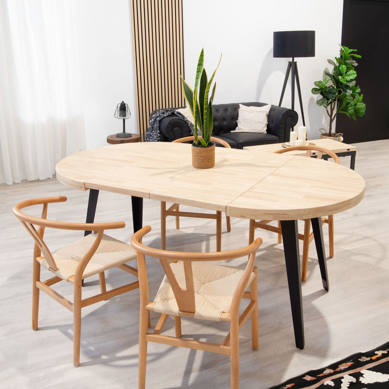 Conjunto de comedor de madera clara con cuatro sillas, sofá negro y lámpara.