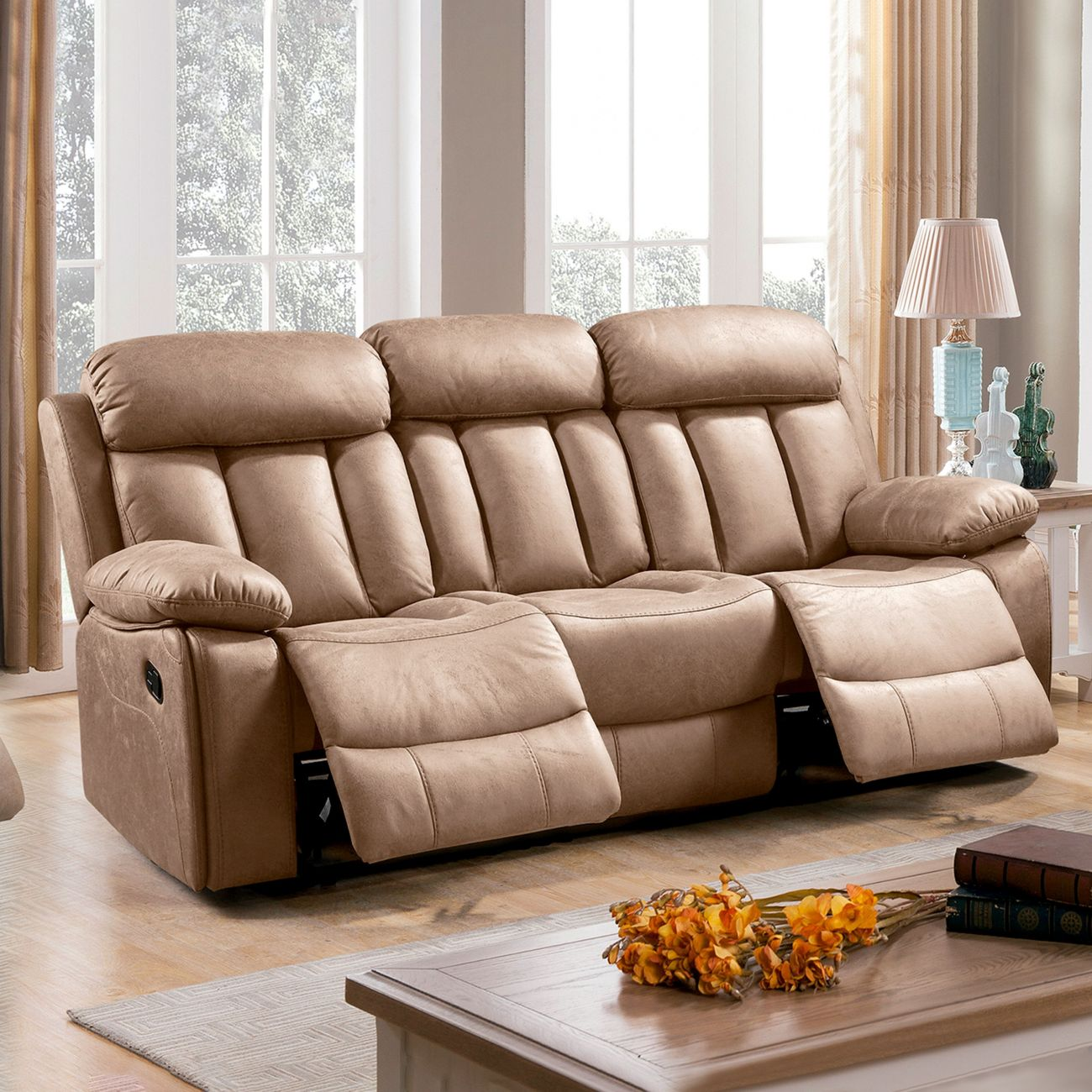 Un sofá beige de 3 plazas con reposapiés extendidos frente a una ventana.