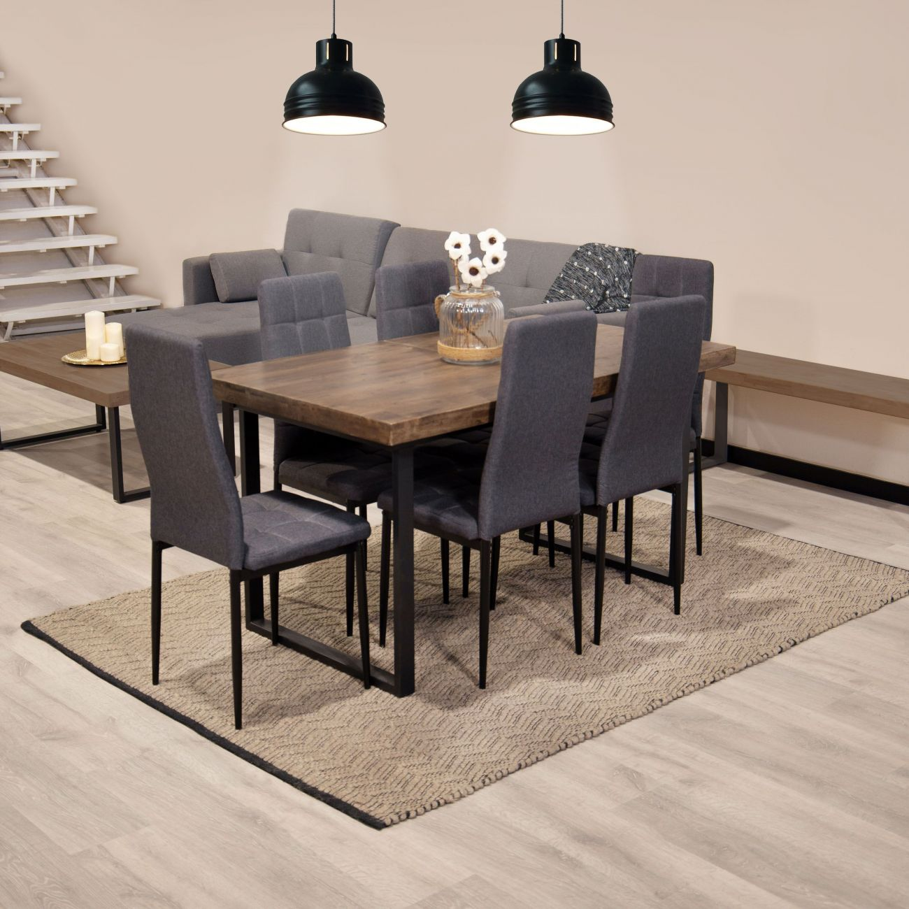 Moderna área de comedor con mesa de madera, sillas grises, sofá y escaleras.