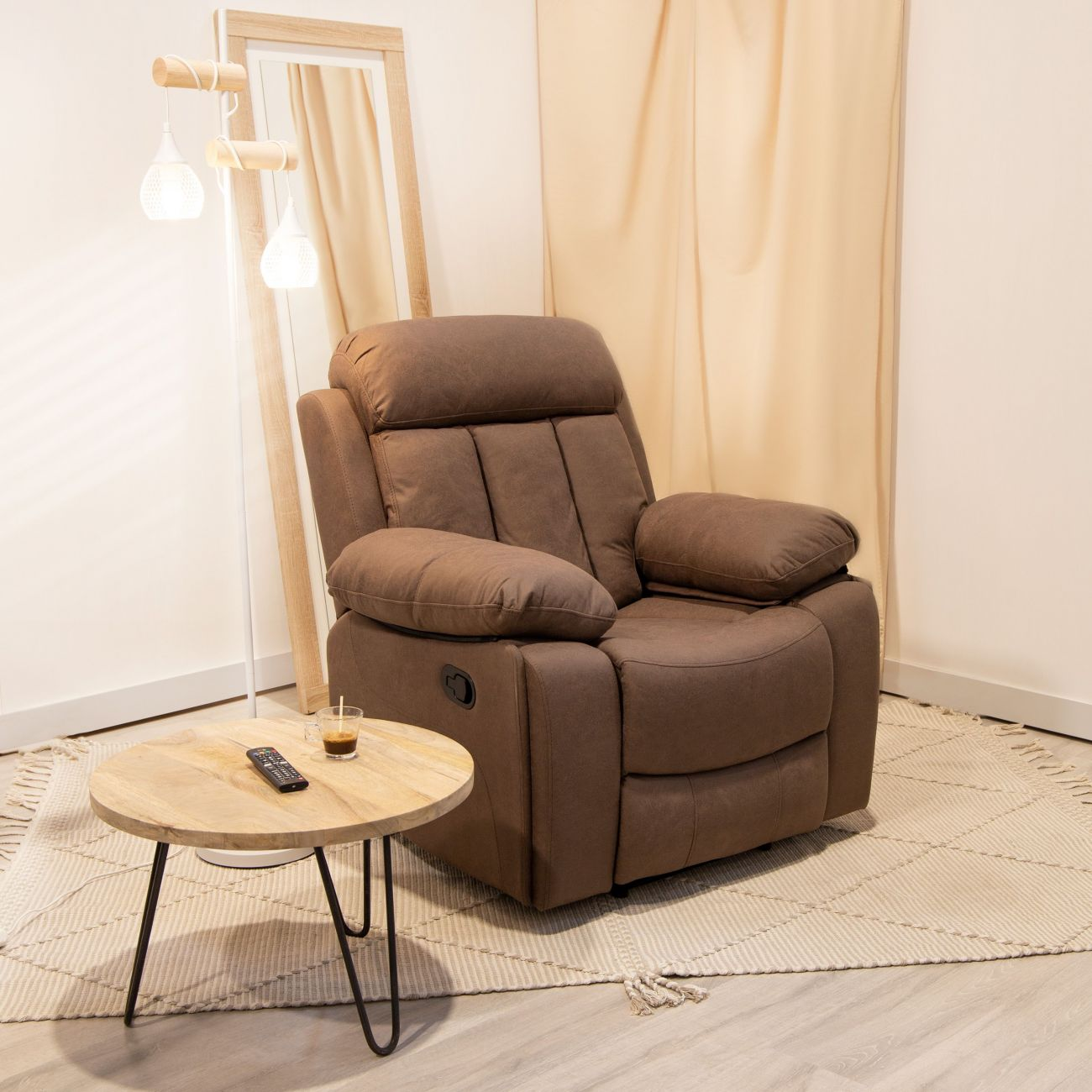 Un sillón reclinable marrón junto a una mesa redonda de madera con un mando y un café.
