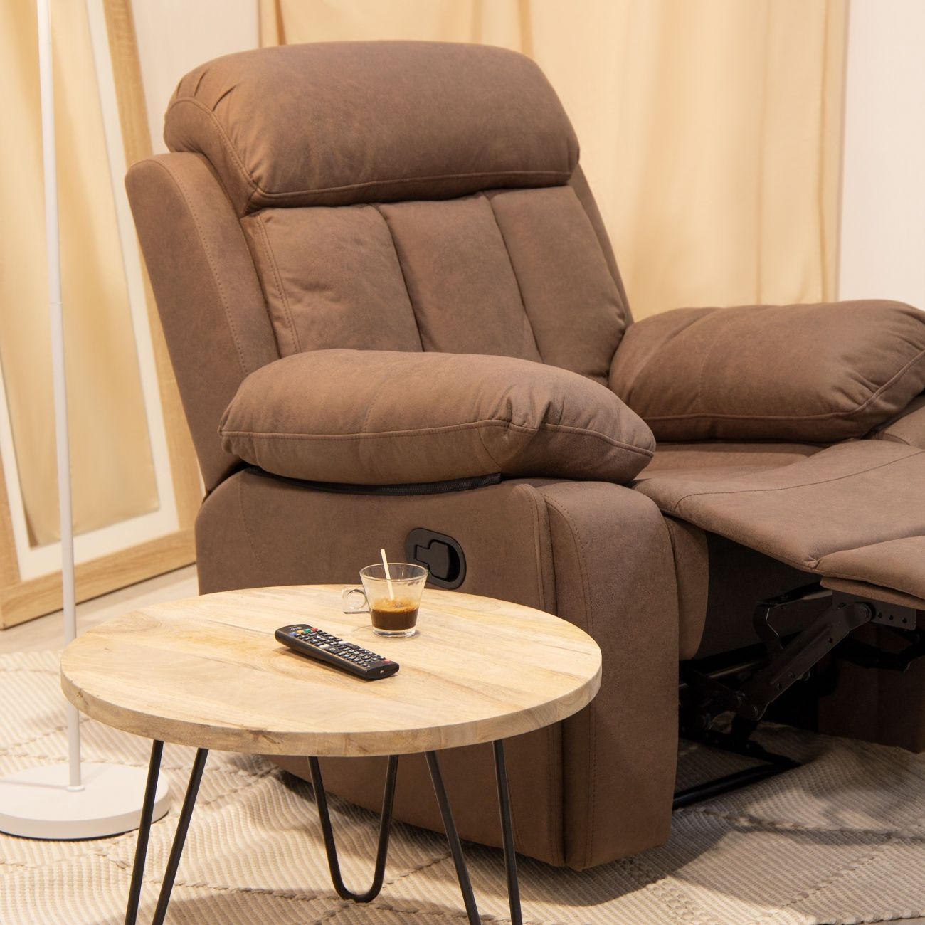 Un sillón reclinable marrón con taza de café y mando en mesa de madera.