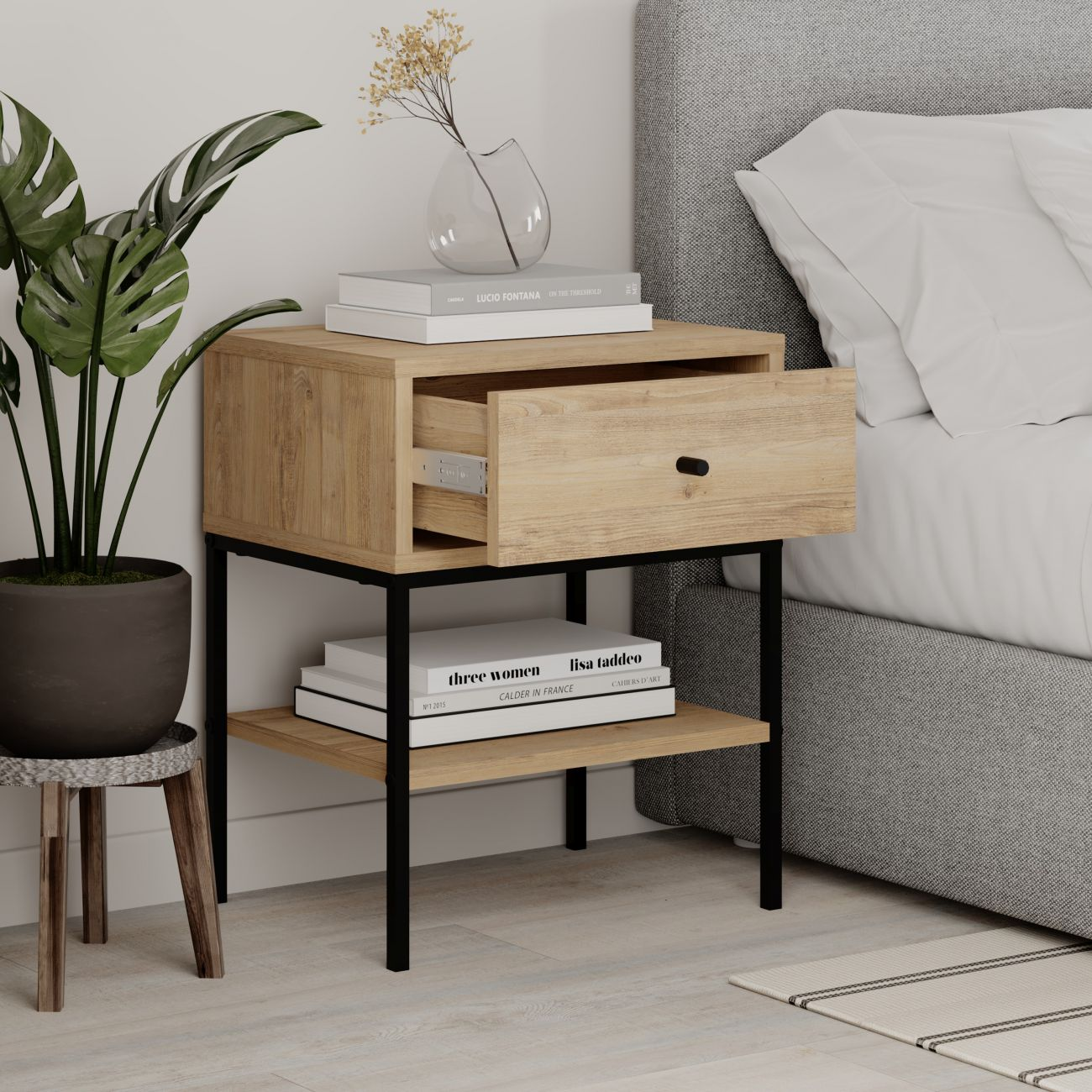 Mesita de noche de madera con cajón abierto, junto a una planta y una cama.