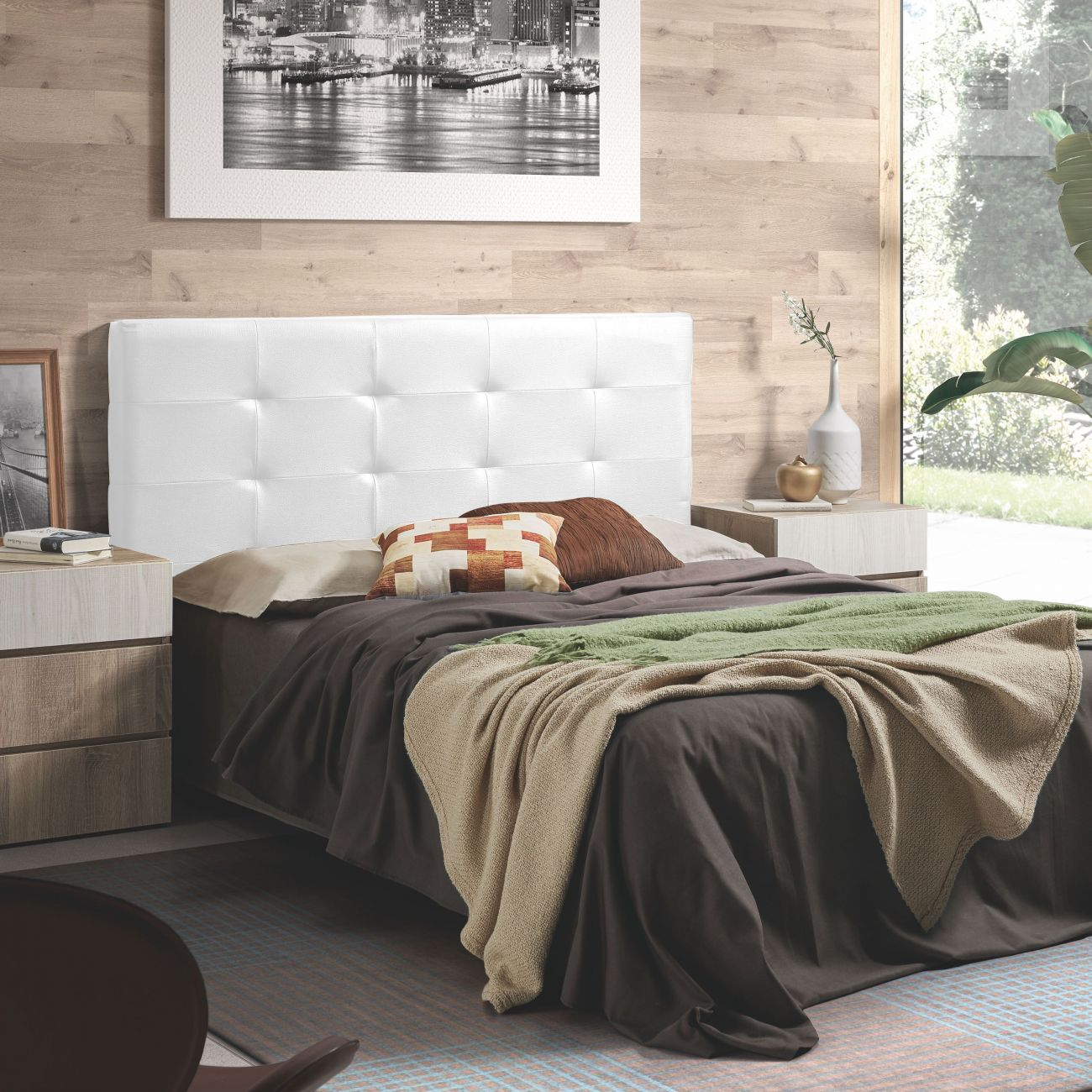Un dormitorio con cabecero blanco, ropa de cama oscura, dos mantas y almohadas.