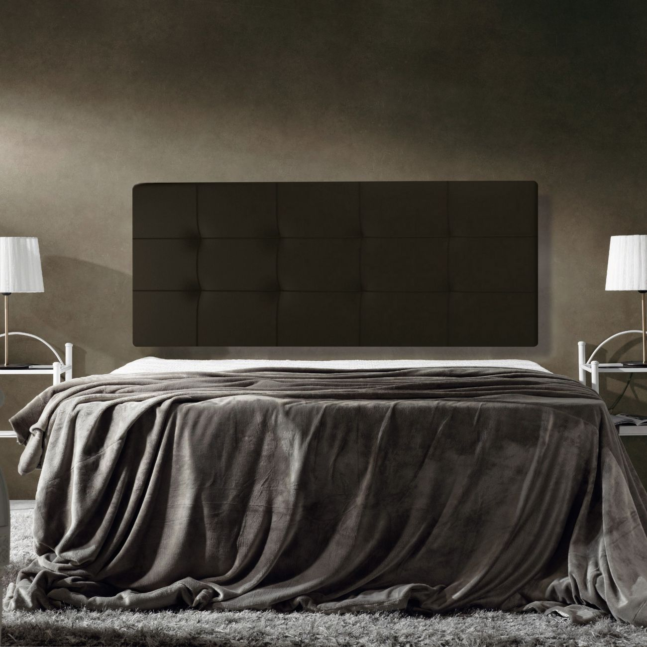 Una cama con cabecero oscuro, manta gris y mesitas de noche con lámparas.