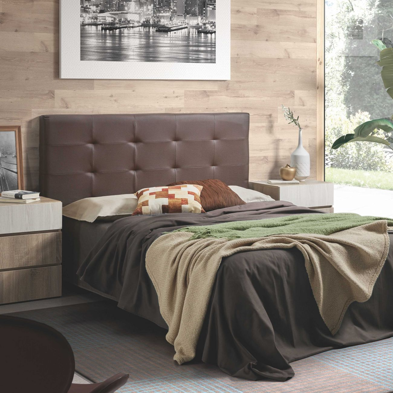 Un dormitorio con cabecero de cuero marrón, ropa de cama gris y verde, mesitas de noche y un cuadro.