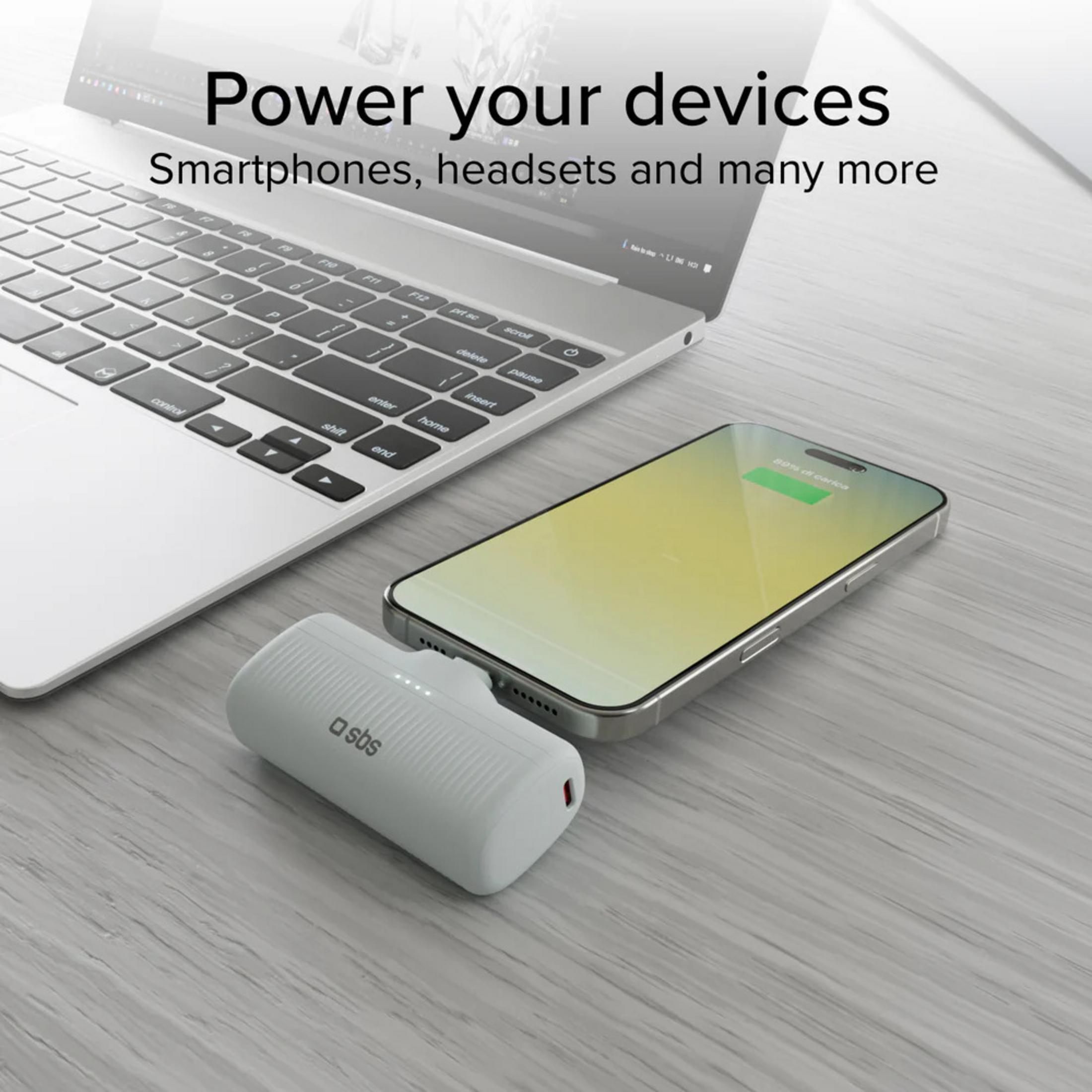 Biały power bank ładuje smartfon obok otwartego laptopa.