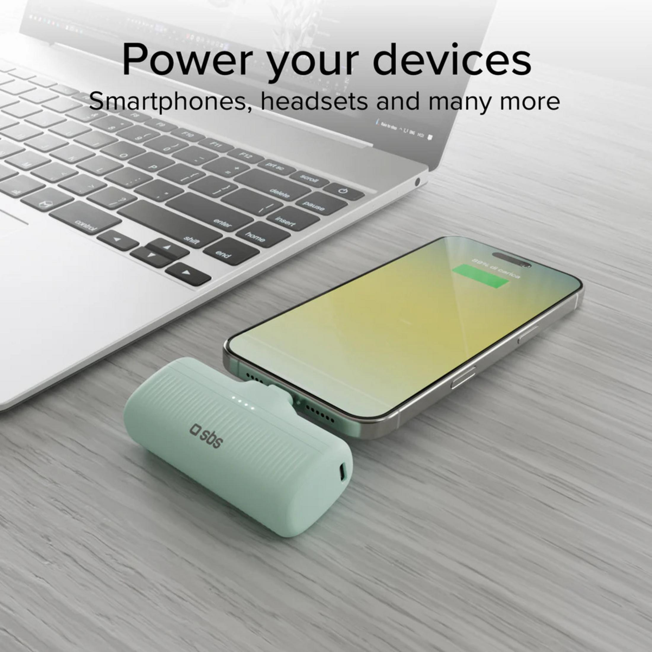 Un power bank verde menta carica uno smartphone accanto a un laptop.