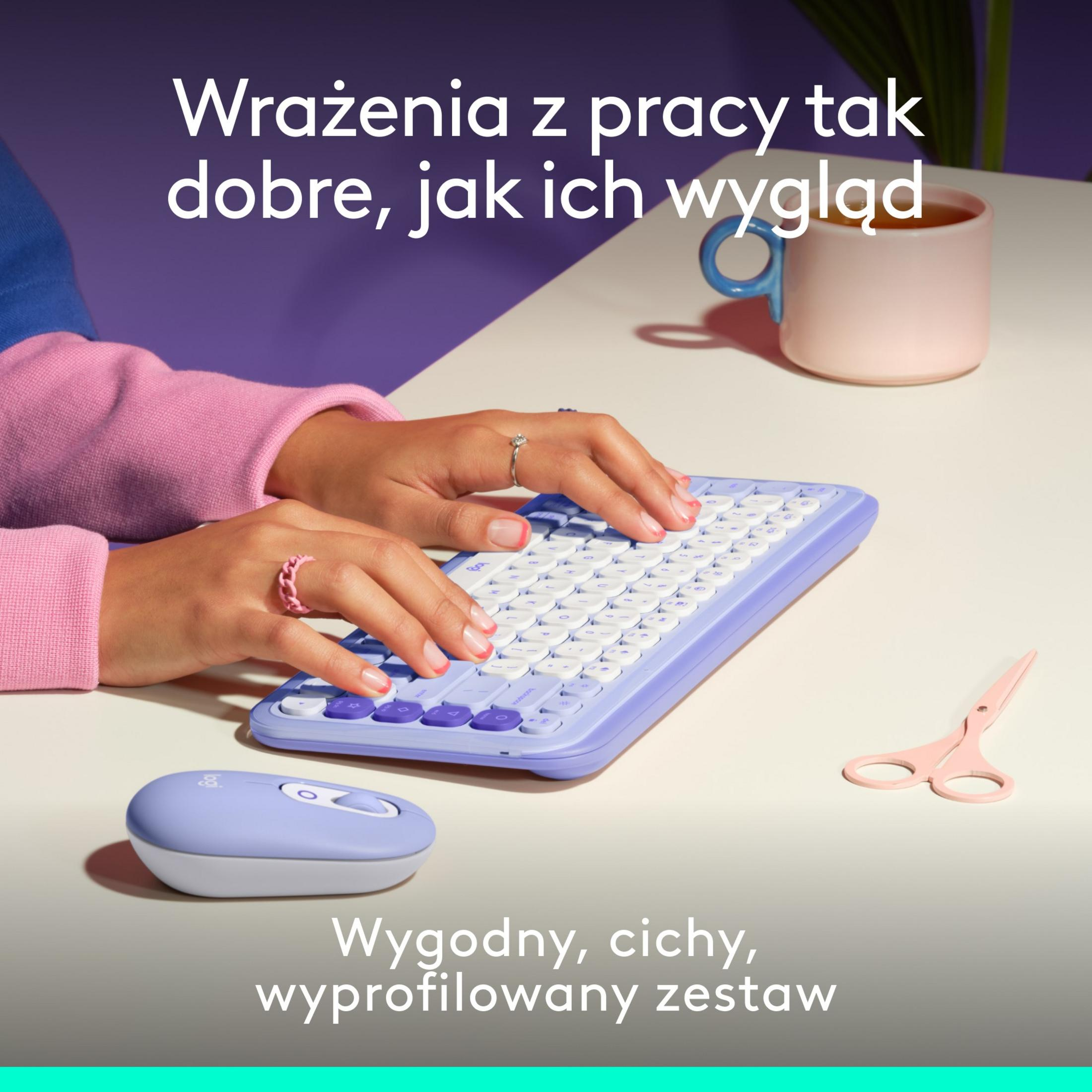Ręce piszą na fioletowej klawiaturze, obok mysz i filiżanka.