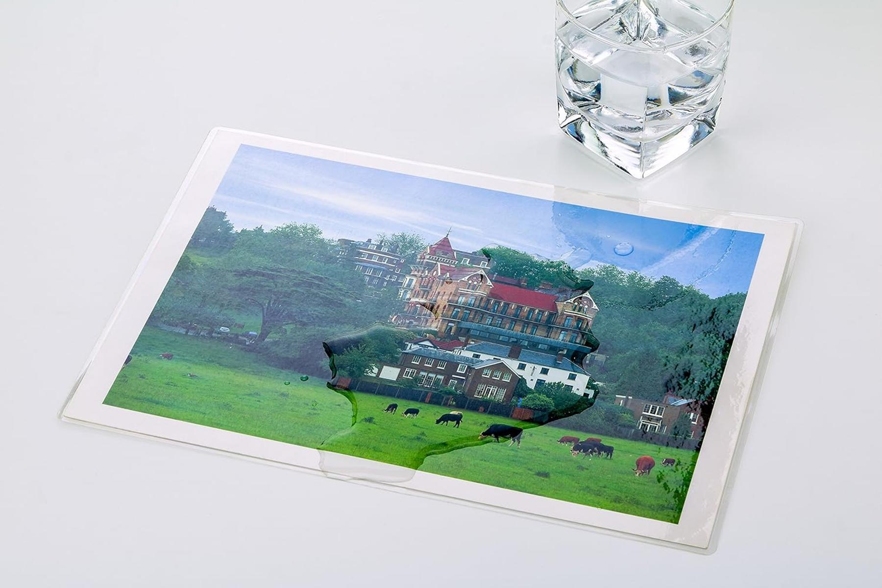 Ein Glas Wasser steht neben einem Bild von Gebäuden auf einer grünen Wiese mit Kühen.