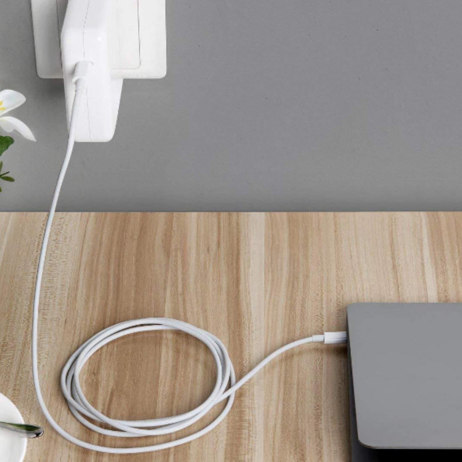 Ein weißes Ladekabel verbindet ein Netzteil mit einem Laptop auf einem Holztisch.