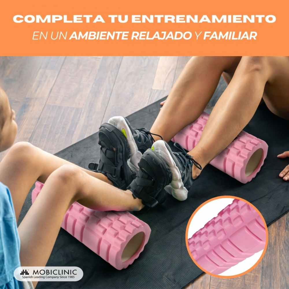 Dos personas usan rodillos de espuma rosas en las piernas sobre una esterilla.