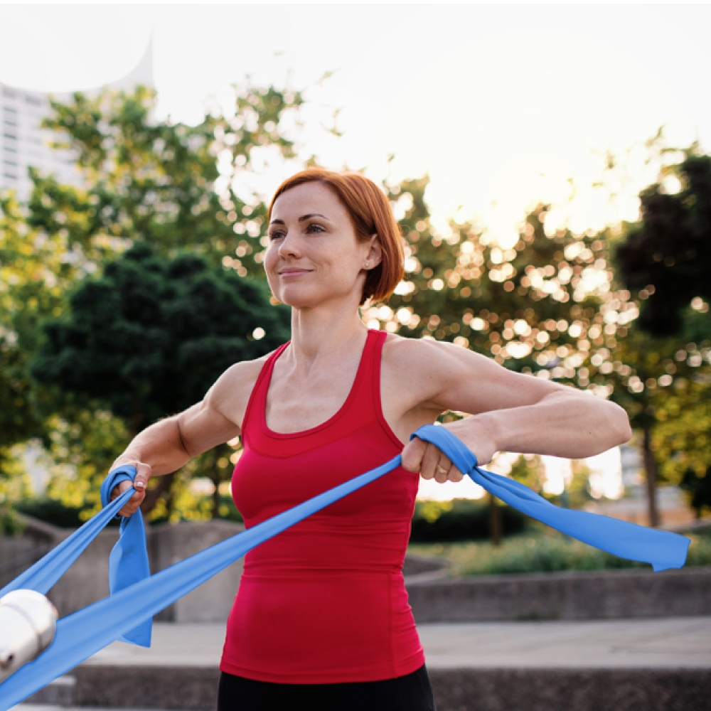 Mujer pelirroja haciendo ejercicio con banda elástica azul al aire libre.