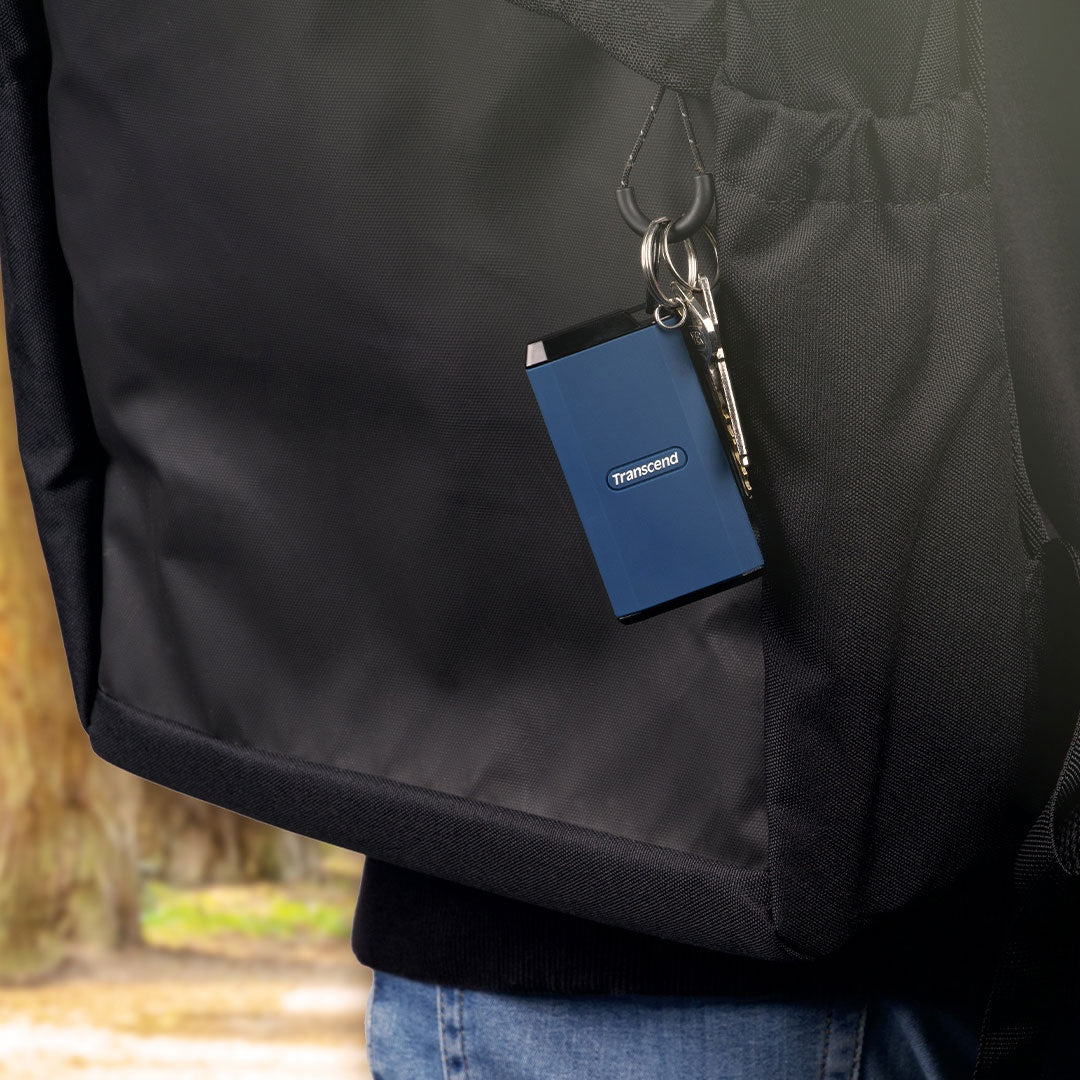Niebieski dysk Transcend z kluczami wisi na czarnym plecaku.