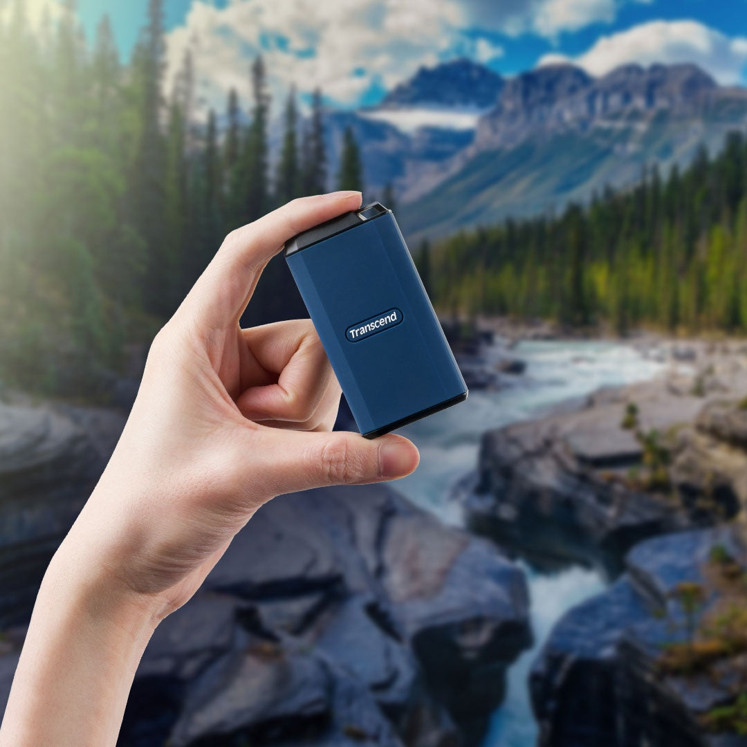 Dłoń trzyma niebieski dysk Transcend na tle górskiego krajobrazu z rzeką.