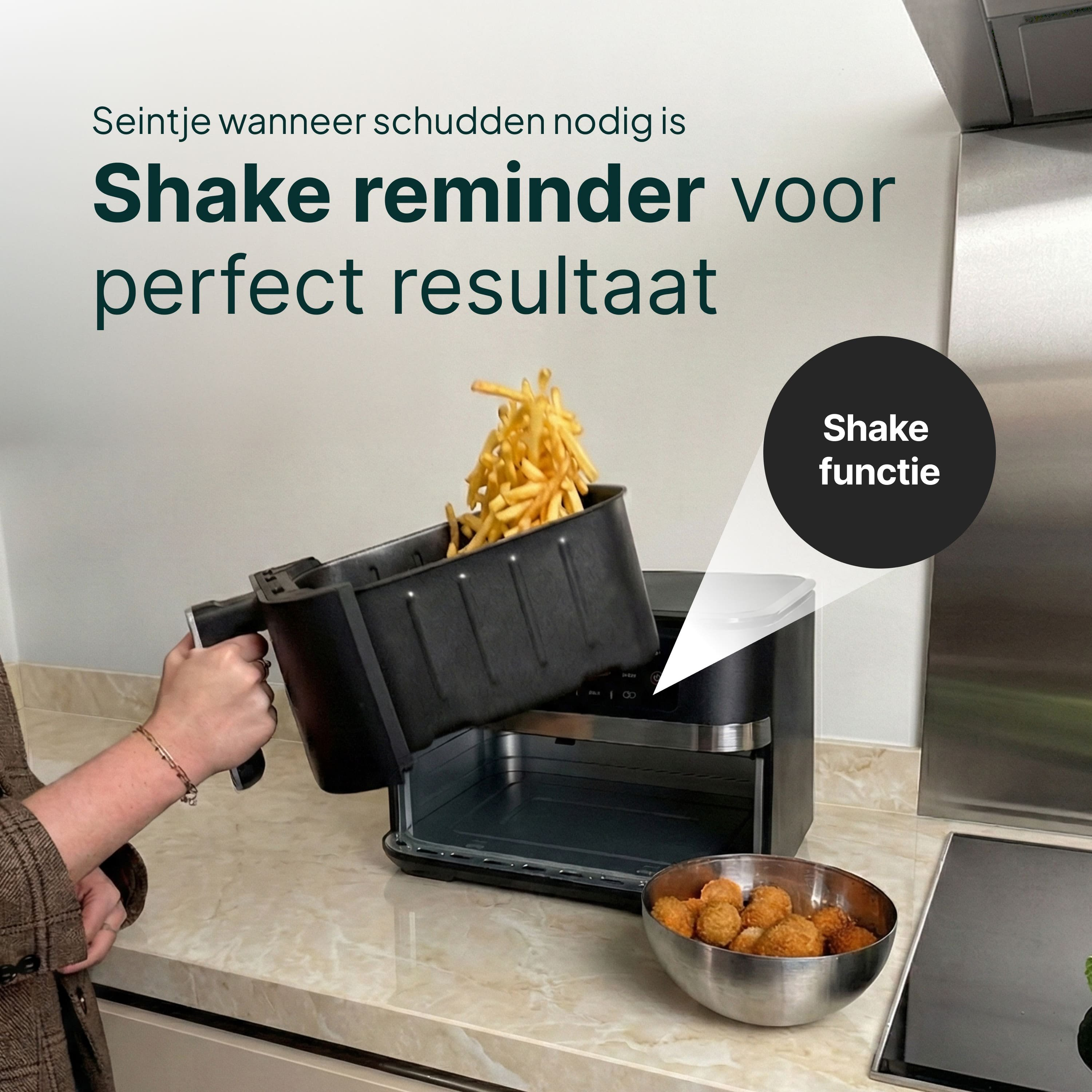 Een hand schudt friet uit een airfryer mand. Snack bowl ernaast.