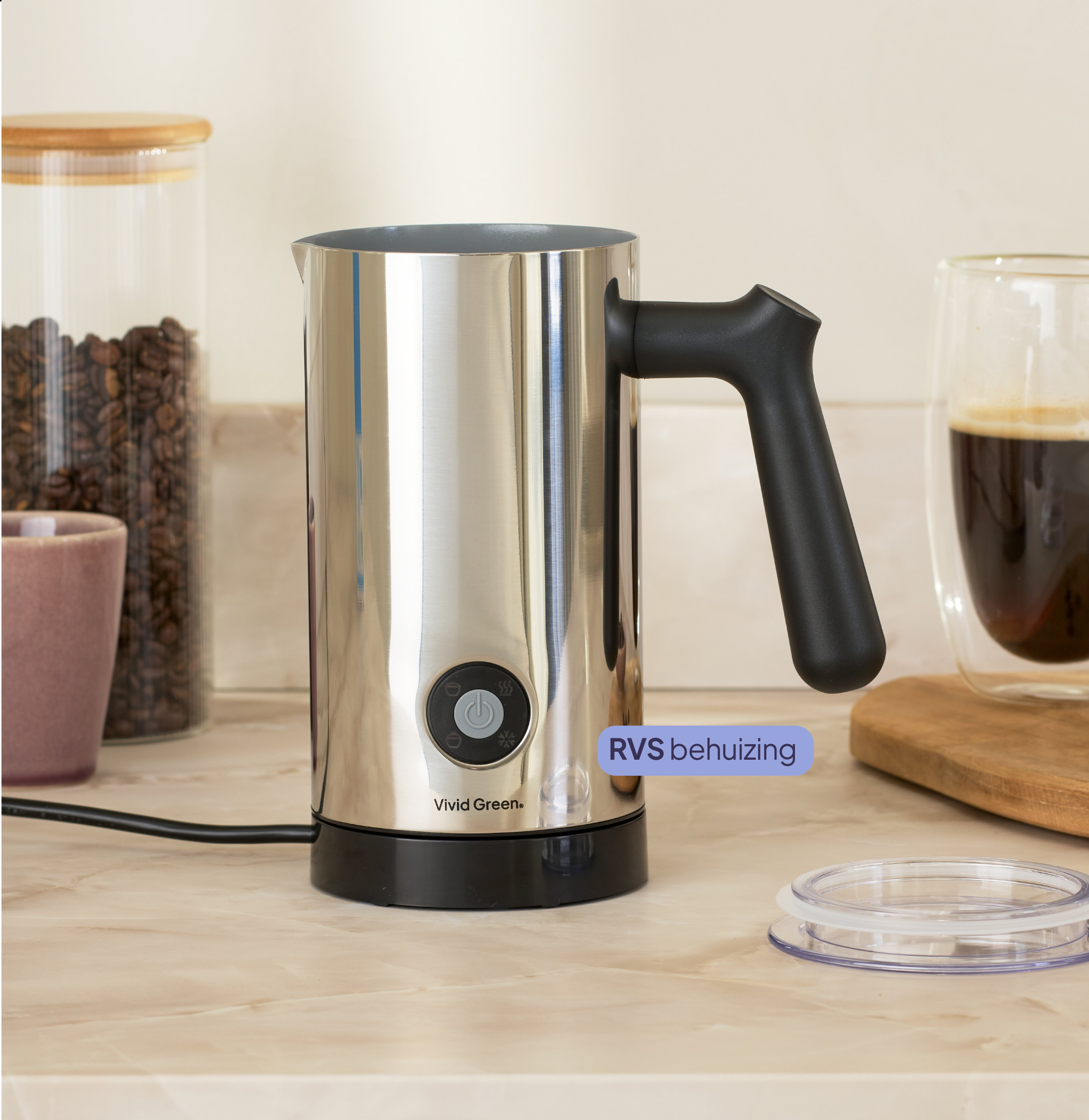 A silver milk frother with a black handle sits on a counter next to coffee beans.
