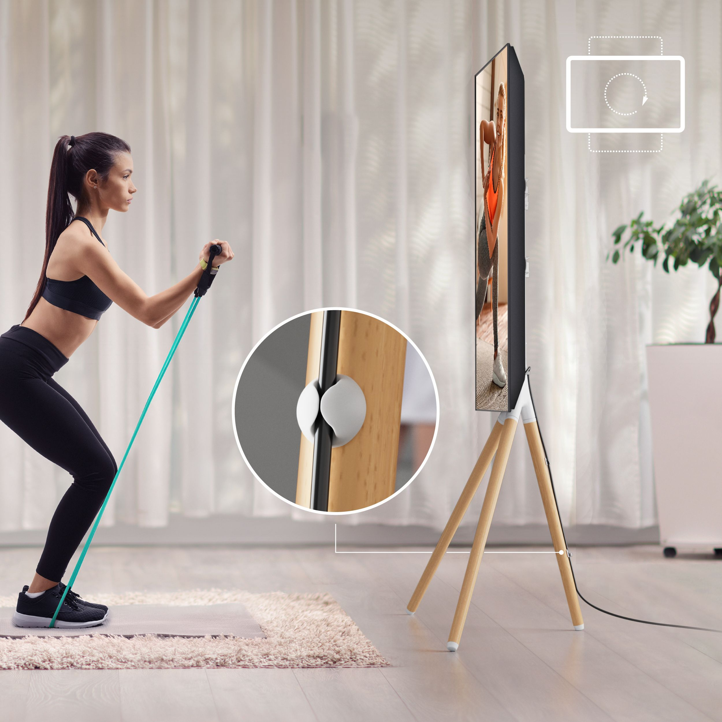 Kobieta ćwiczy z gumą przed telewizorem na statywie.