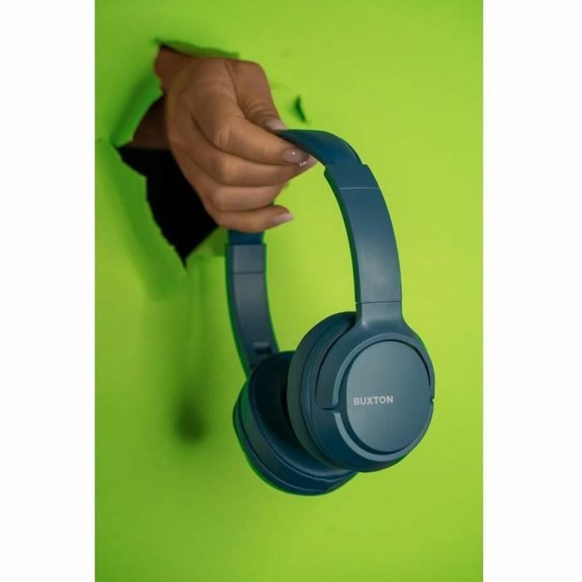Una mano tiene cuffie blu attraverso un buco in un tessuto verde.