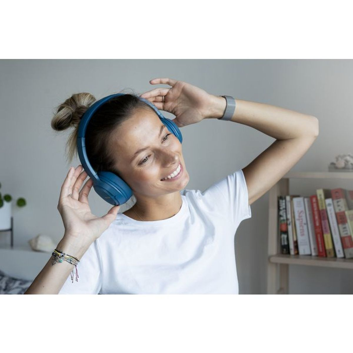 Una donna con cuffie blu e maglietta bianca sorride.