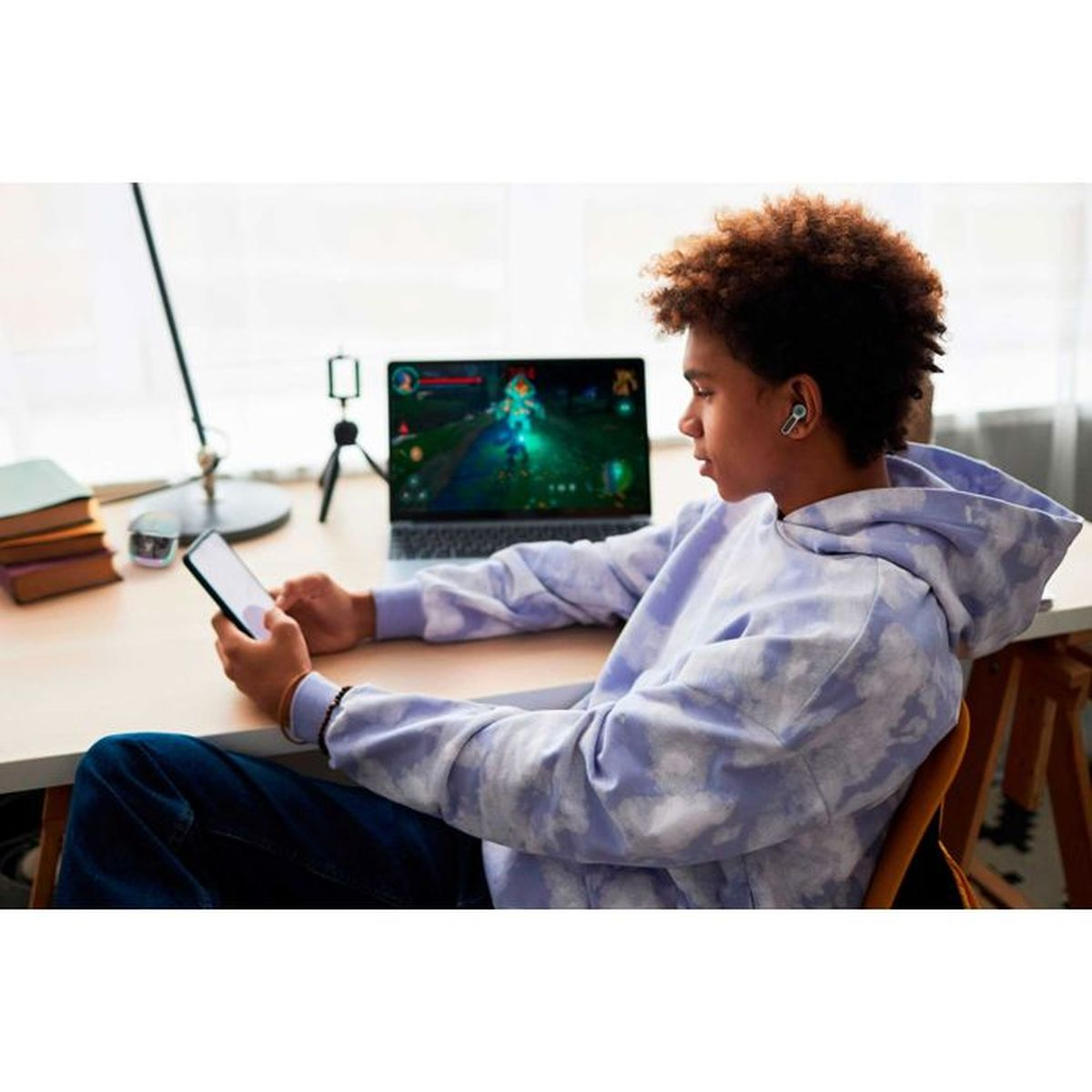 Junge mit Kopfhörern spielt Videospiel auf Laptop, hält Smartphone in der Hand.
