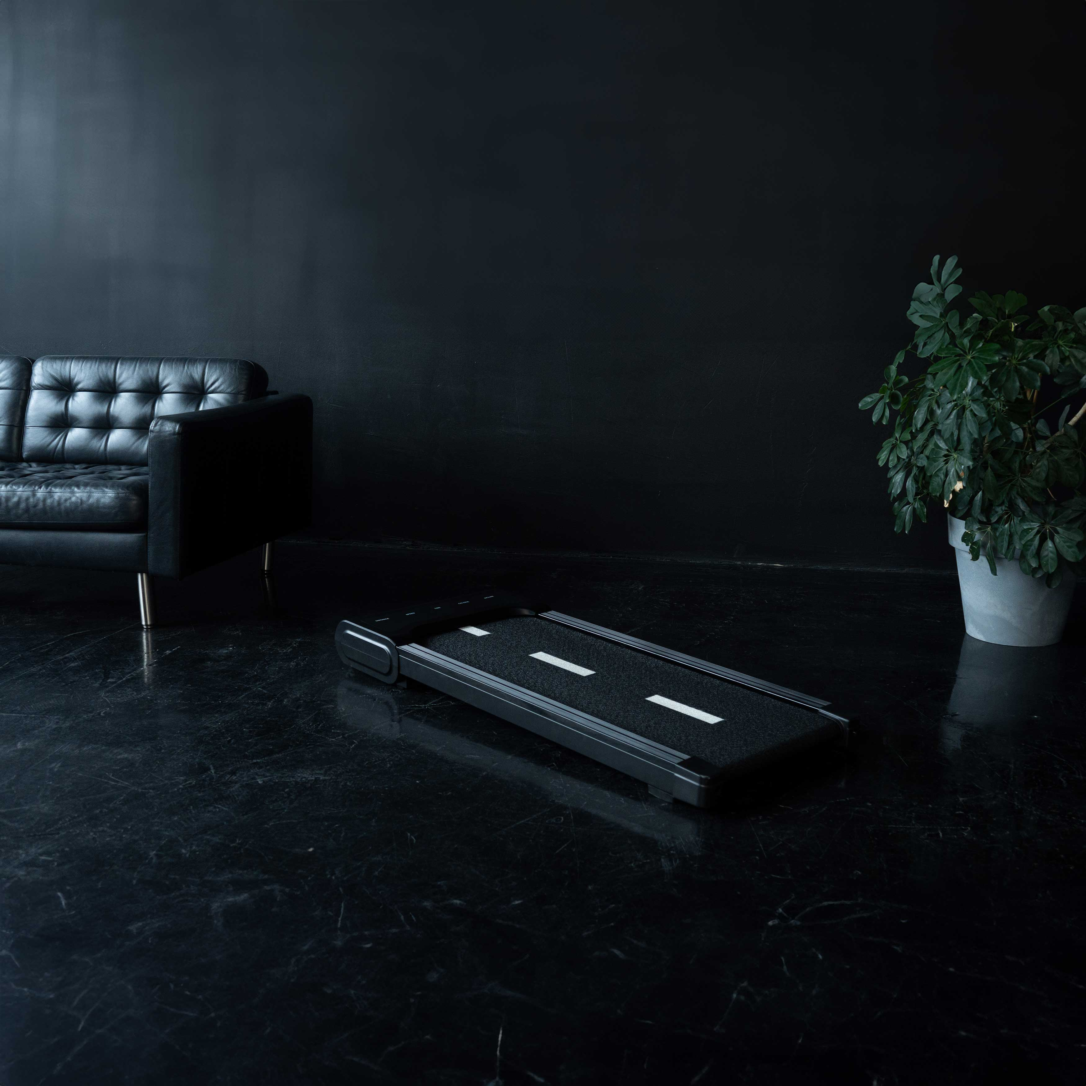 Czarna bieżnia z białymi liniami na ciemnym marmurowym podłodze obok sofy.