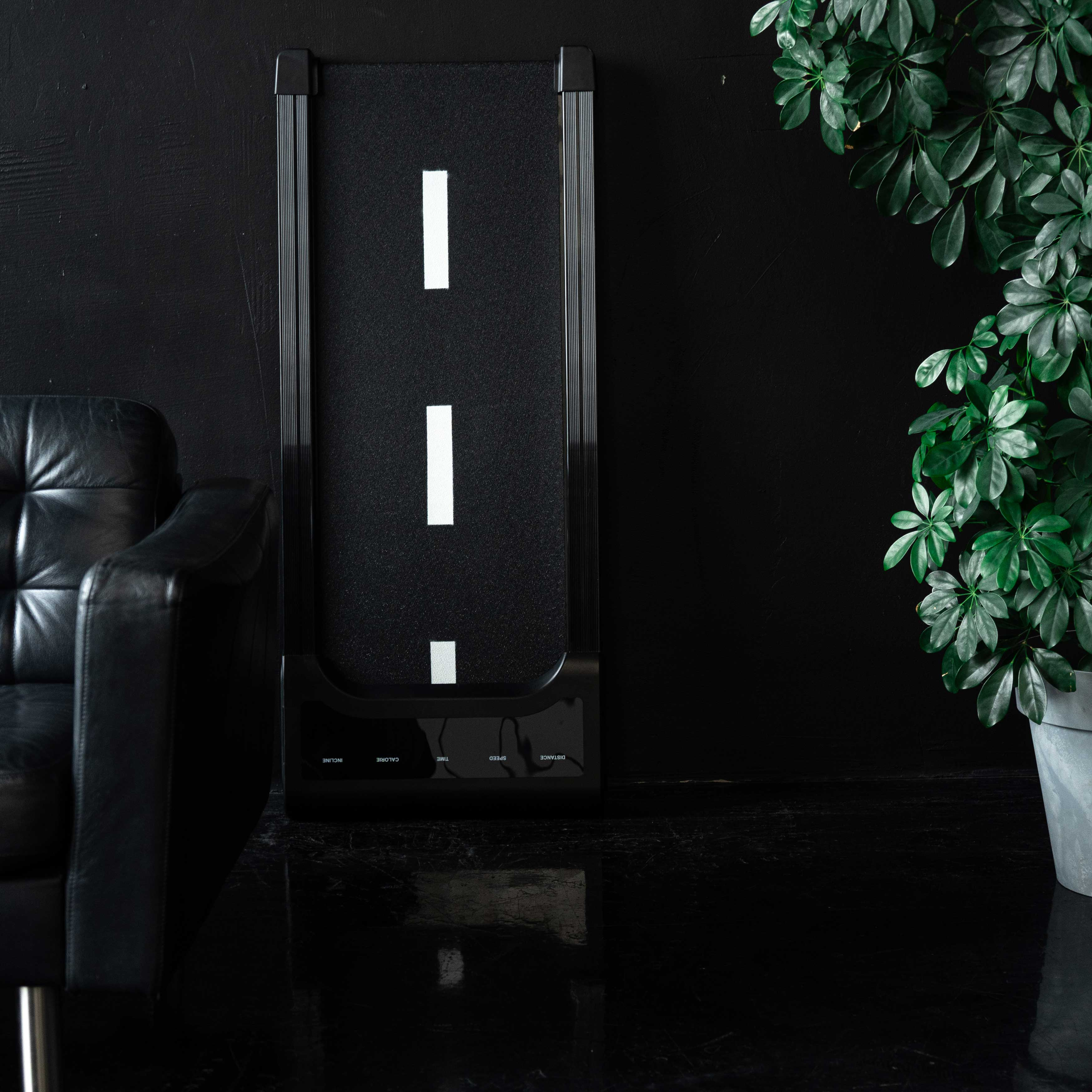 Czarny fotel obok bieżni z białymi paskami i zieloną rośliną.