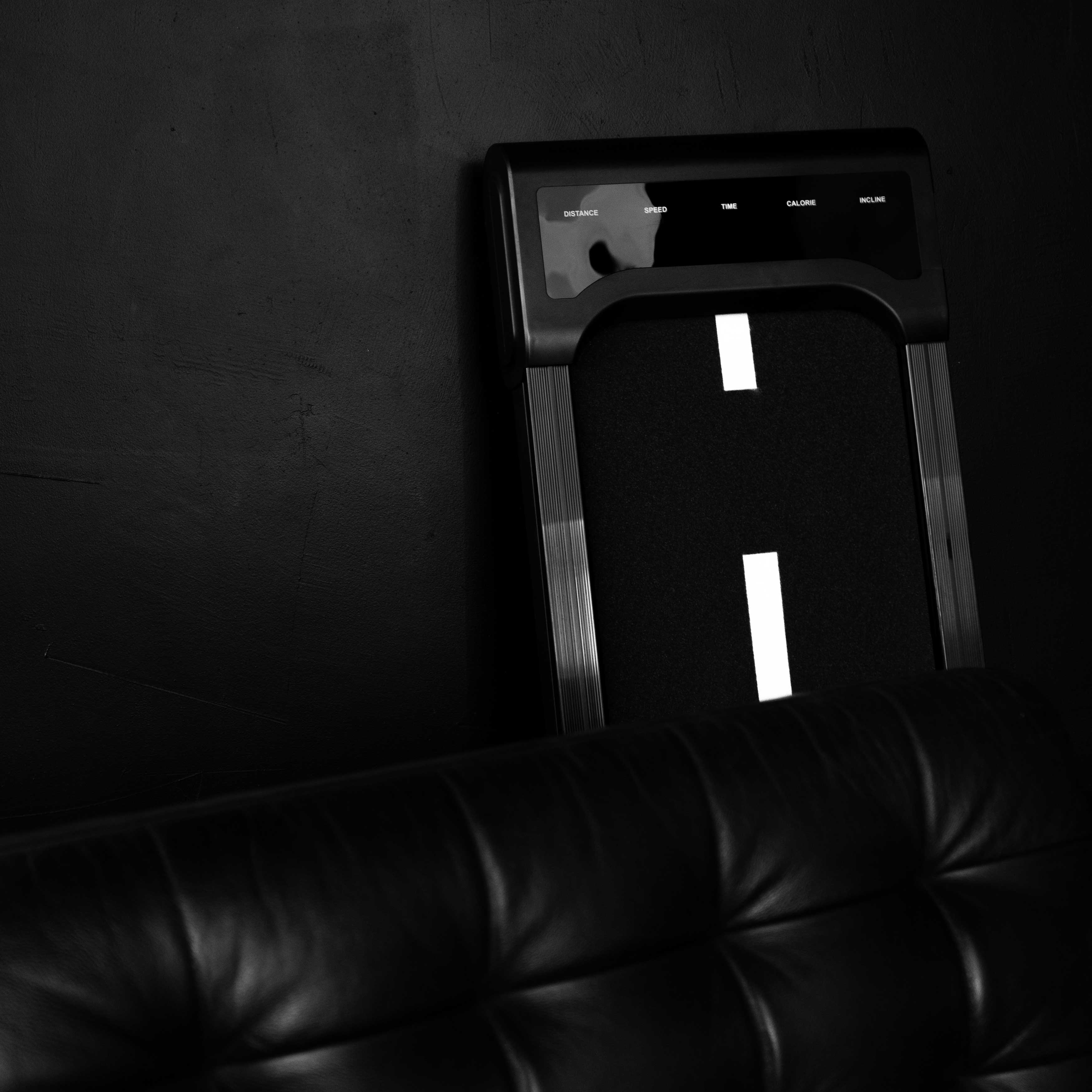Czarna bieżnia z wyświetlaczem i skórzaną ławką obok.