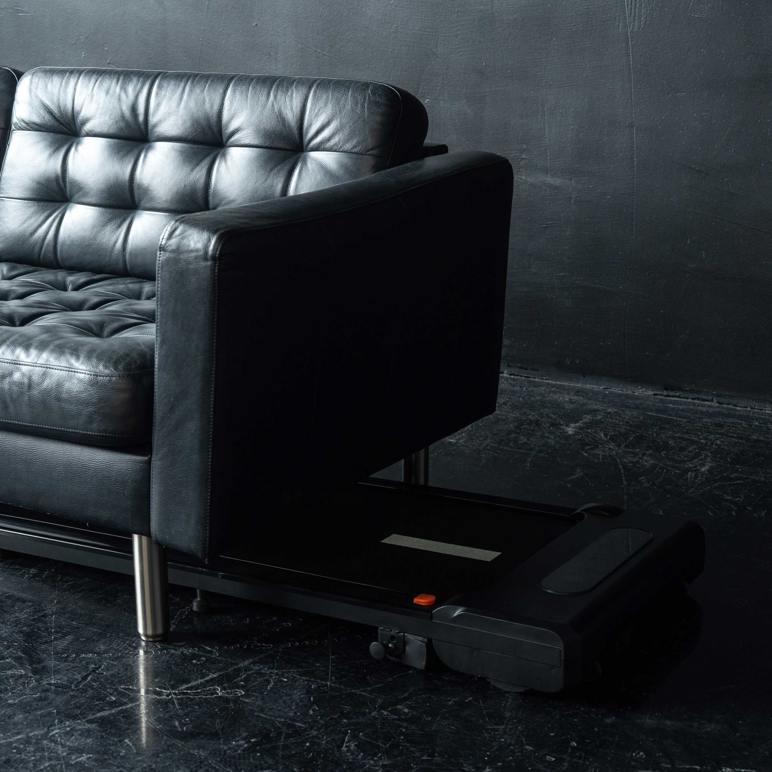 Czarna skórzana kanapa obok czarnej bieżni z pomarańczowym przyciskiem.