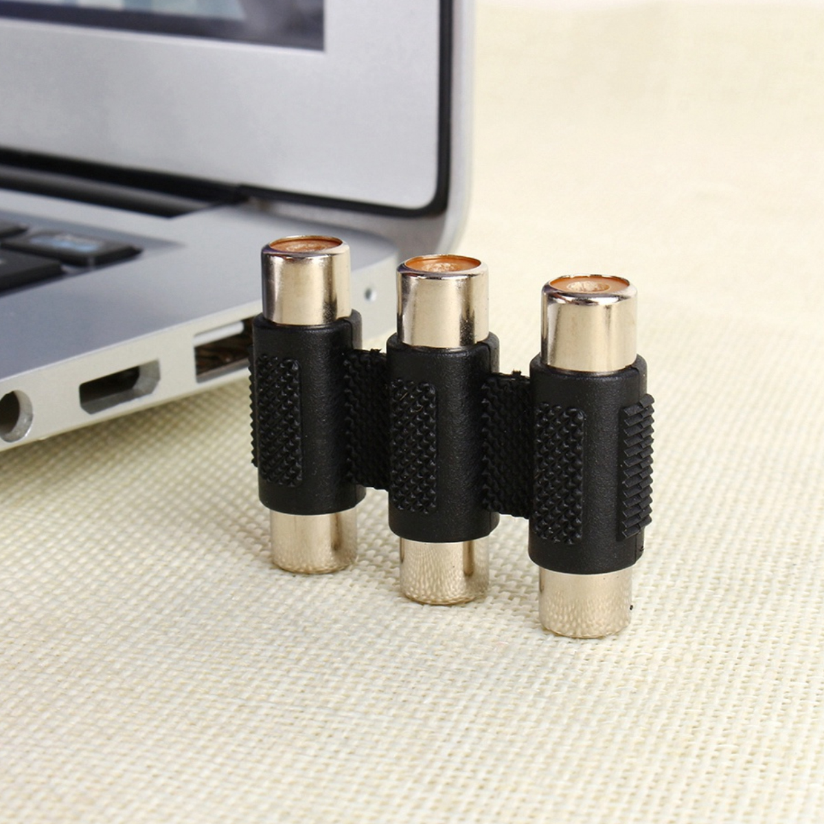 Drei RCA-Adapter nebeneinander, mit einem Laptop im Hintergrund.