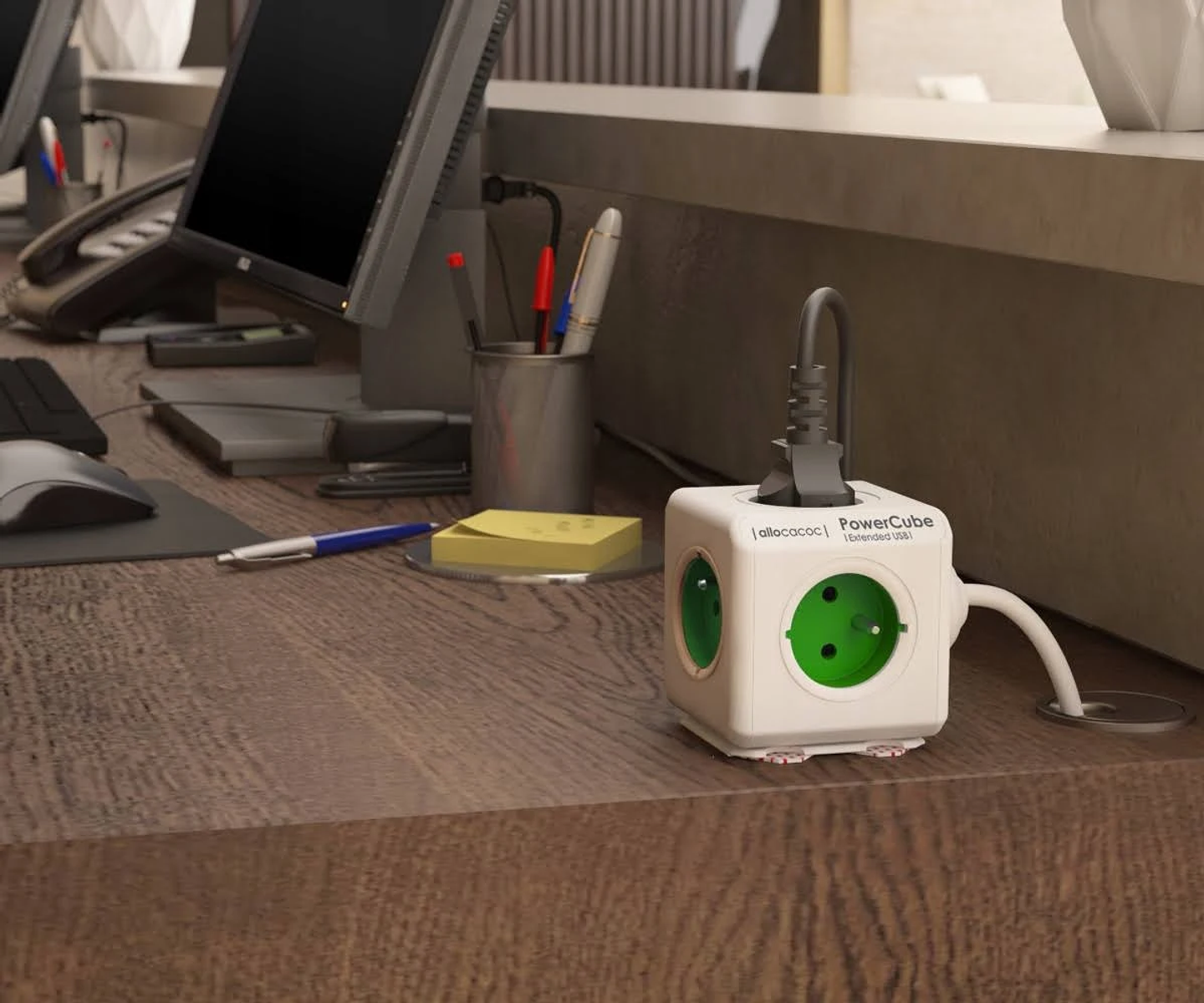 Biała kostka przedłużacza z zielonymi gniazdami stoi na drewnianym biurku.