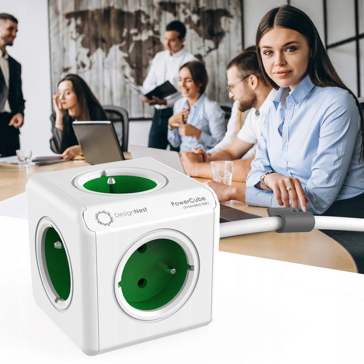 Biały PowerCube z zielonymi gniazdami stoi na stole, ludzie pracują w tle.