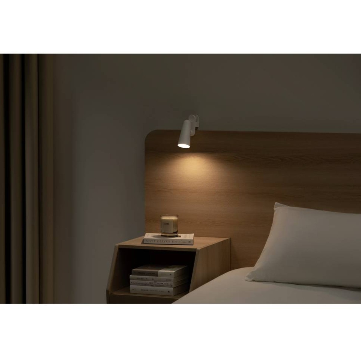Een nachtkastje naast een bed met een fel licht. Boeken en een kaars zijn zichtbaar.