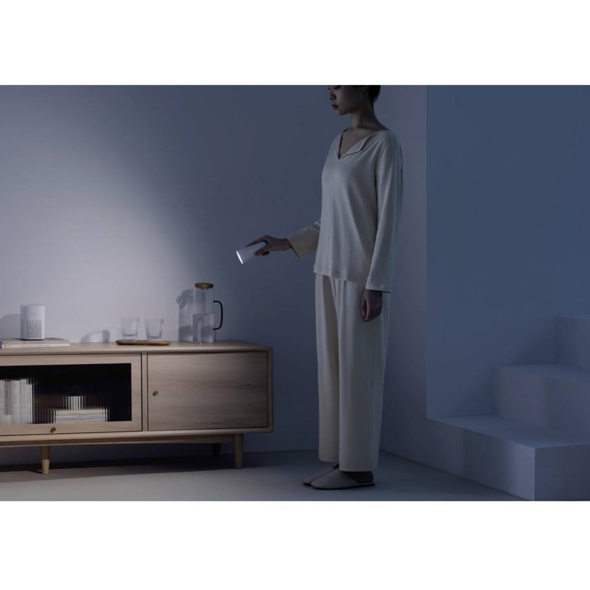 Vrouw in pyjama schijnt met zaklamp op nachtkastje met spullen.