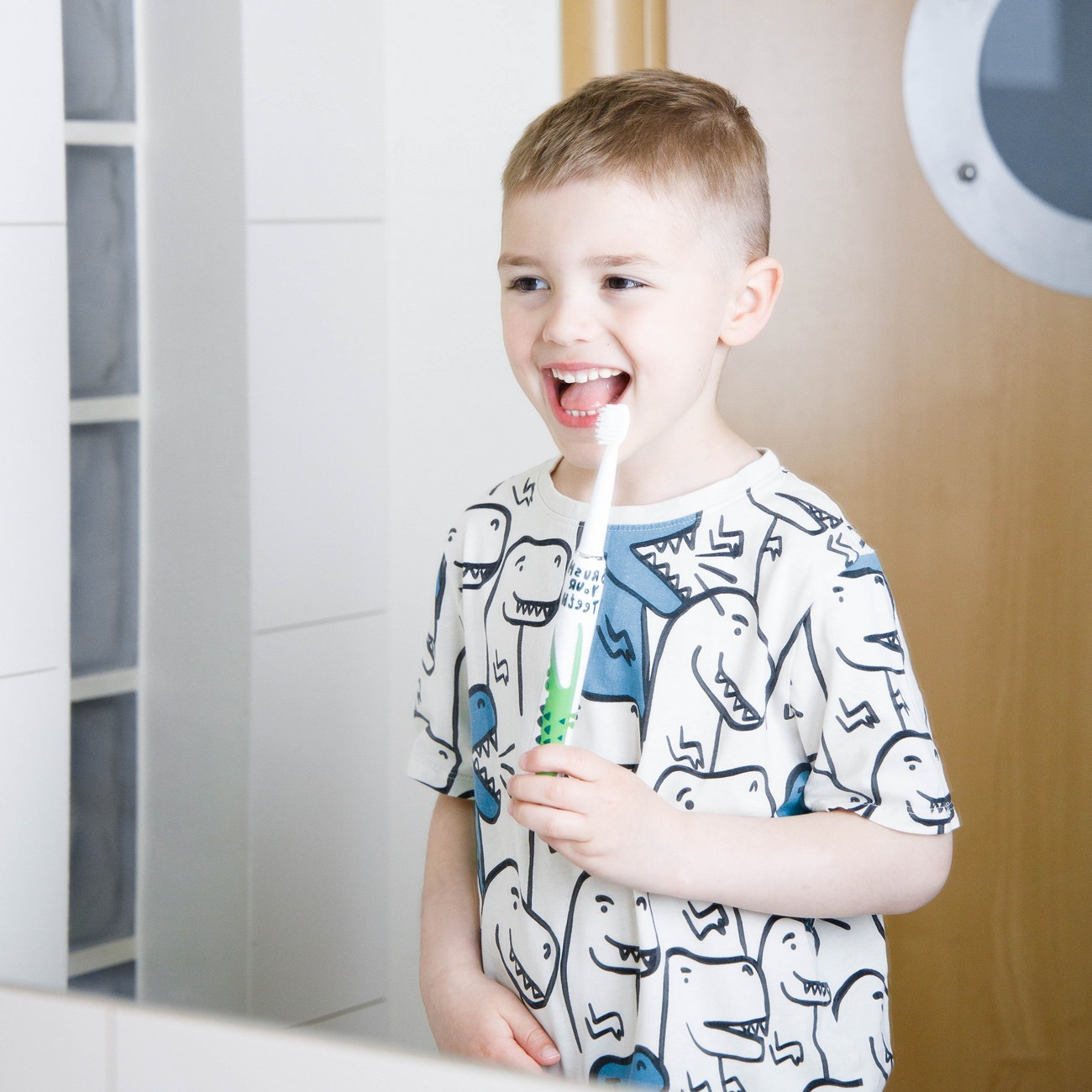 Bambino con spazzolino e maglietta di dinosauro si lava i denti.