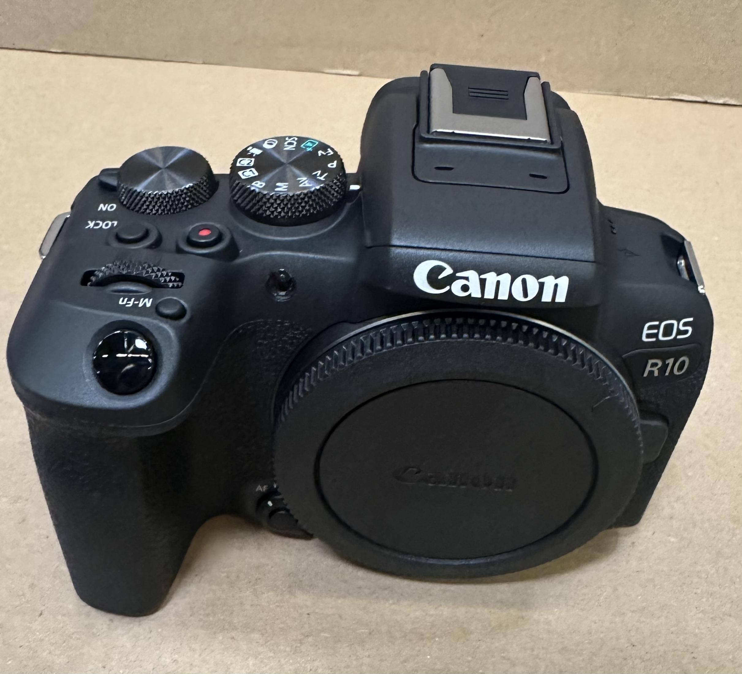 Fotocamera Canon EOS R10 nera con tappo obiettivo e pulsanti di controllo.