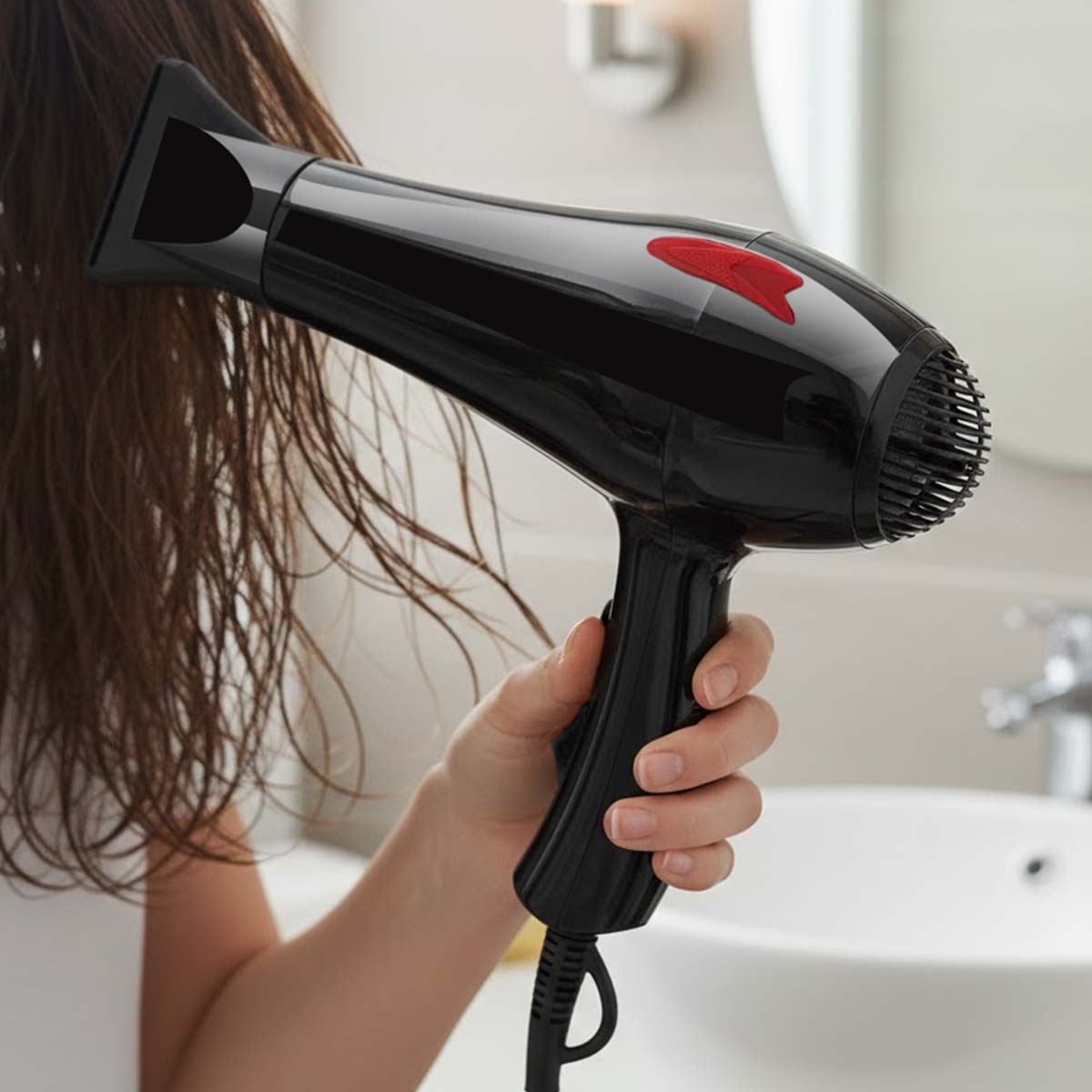 Eine Person trocknet ihr nasses Haar mit einem schwarzen Föhn in einem Badezimmer.