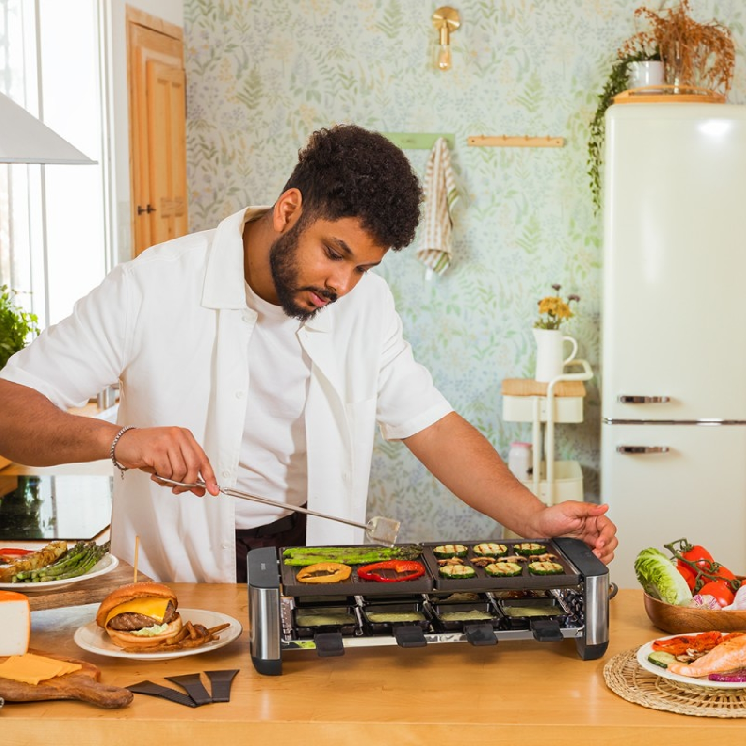 Mężczyzna gotuje warzywa i łososia na grillu raclette z burgerem i szparagami.