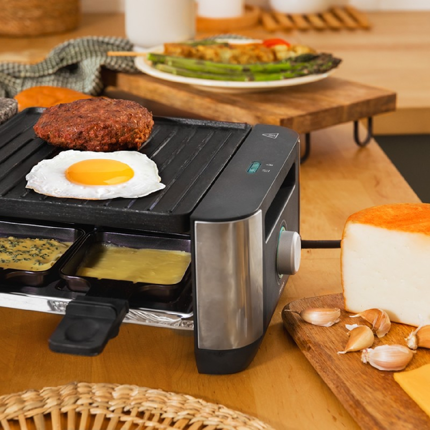 Grill z burgerem i jajkiem, patelnie do raclette, ser i czosnek na drewnianym stole.