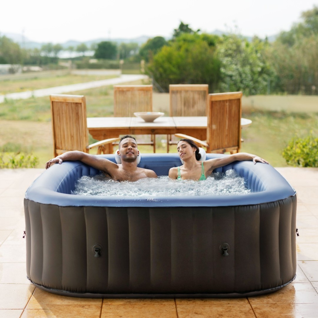 Mann und Frau entspannen in einem aufblasbaren Whirlpool im Freien mit Blick auf eine Terrasse und Landschaft.