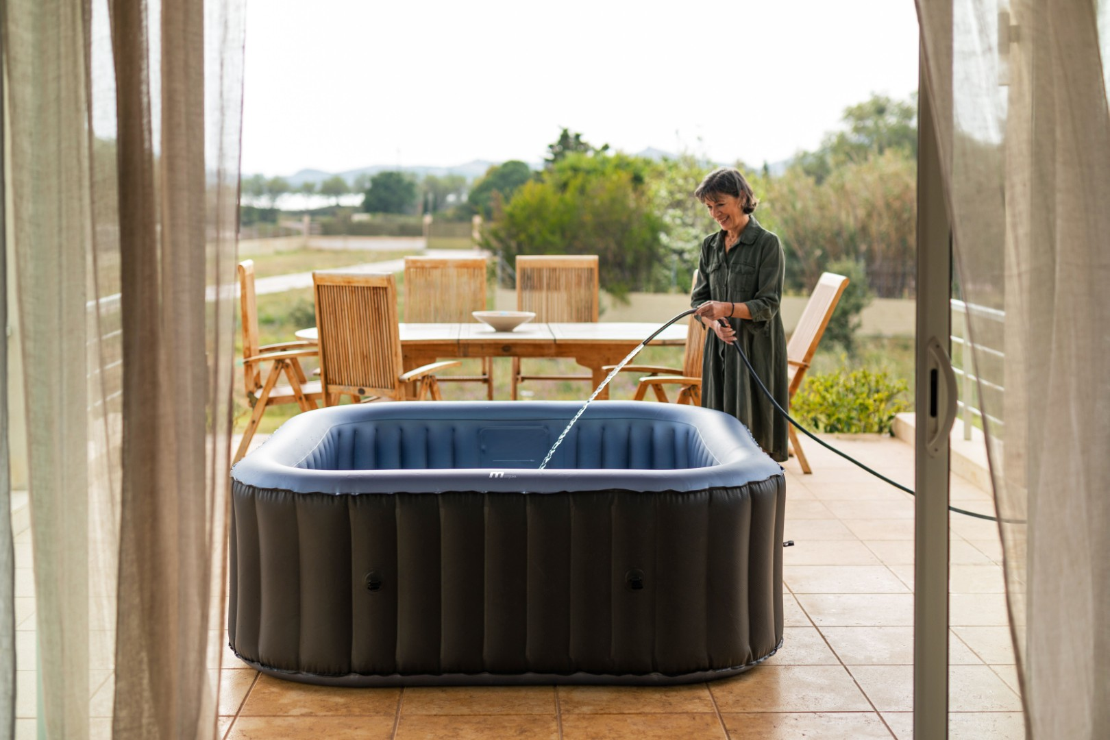 Eine Frau füllt einen aufblasbaren Whirlpool mit einem Schlauch auf einer Terrasse.
