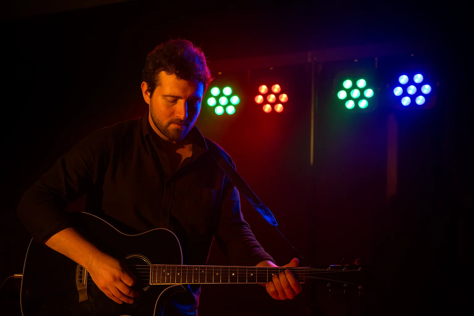 Ein Mann spielt auf einer Akustikgitarre im Schein von roten, grünen und blauen Lichtern.