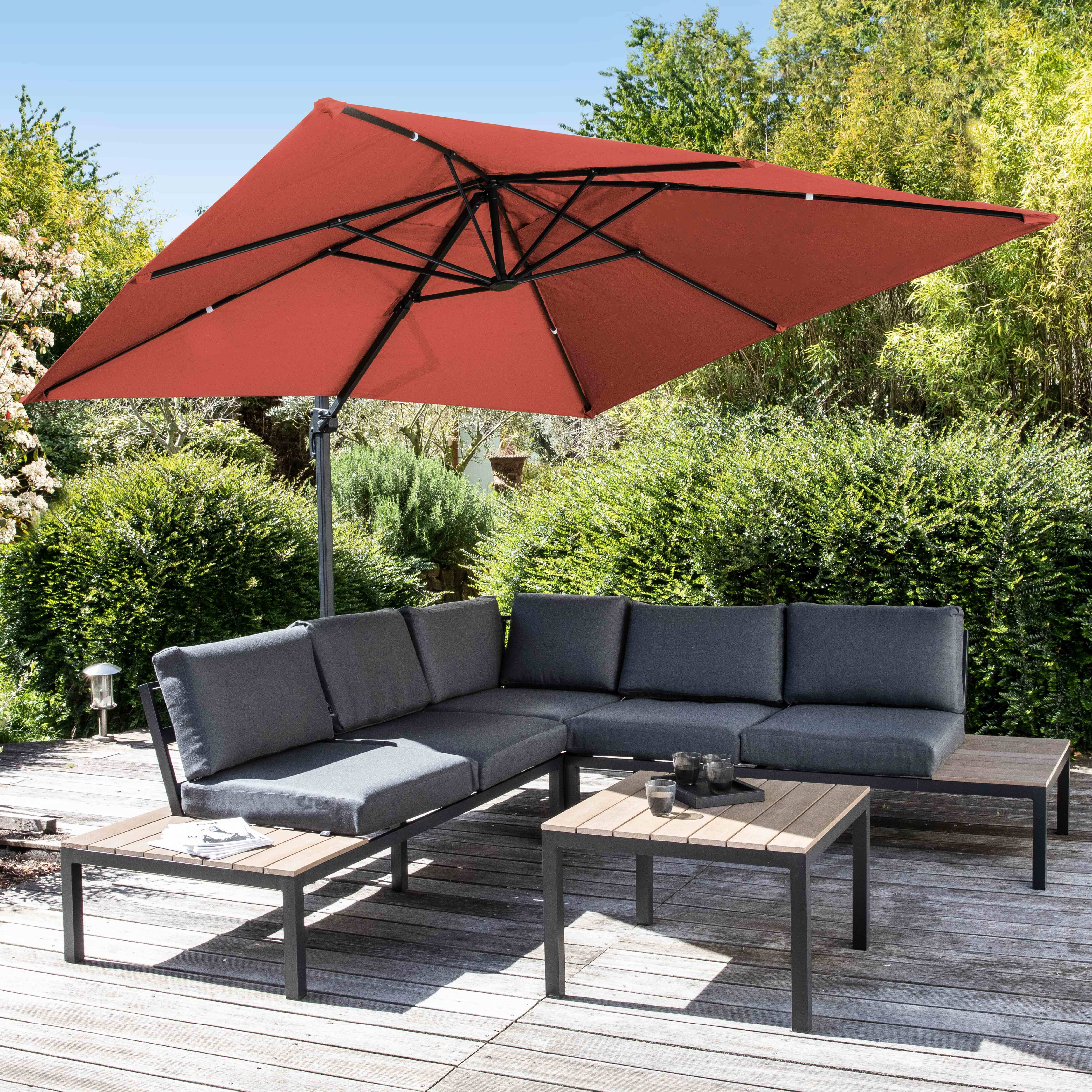Gartenlounge mit L-förmigem Sofa, Couchtischen und rotem Sonnenschirm.