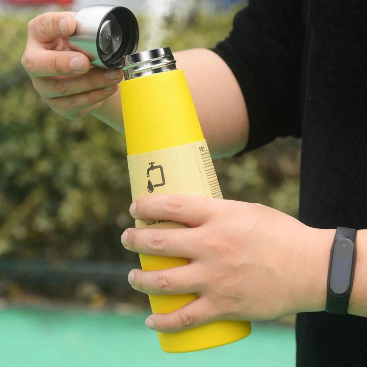 Gelbe Flasche mit Metallsockel wird von Händen gehalten. Deckel wird abgenommen.